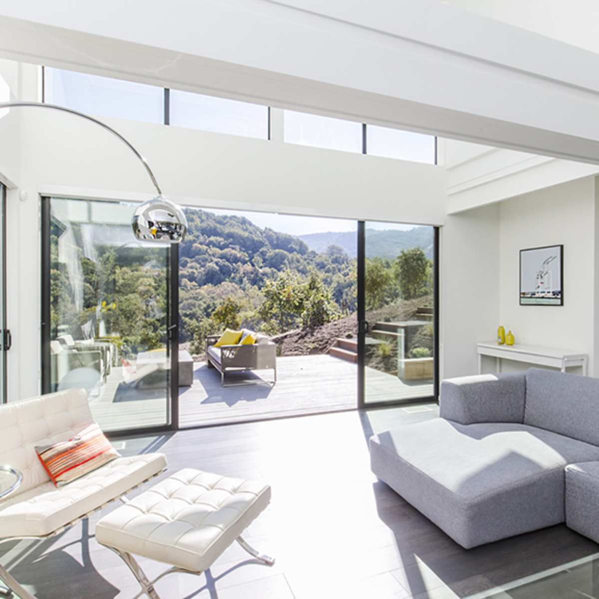 A modern living room features large glass windows that open to a view of grassy hills and outdoor seating.