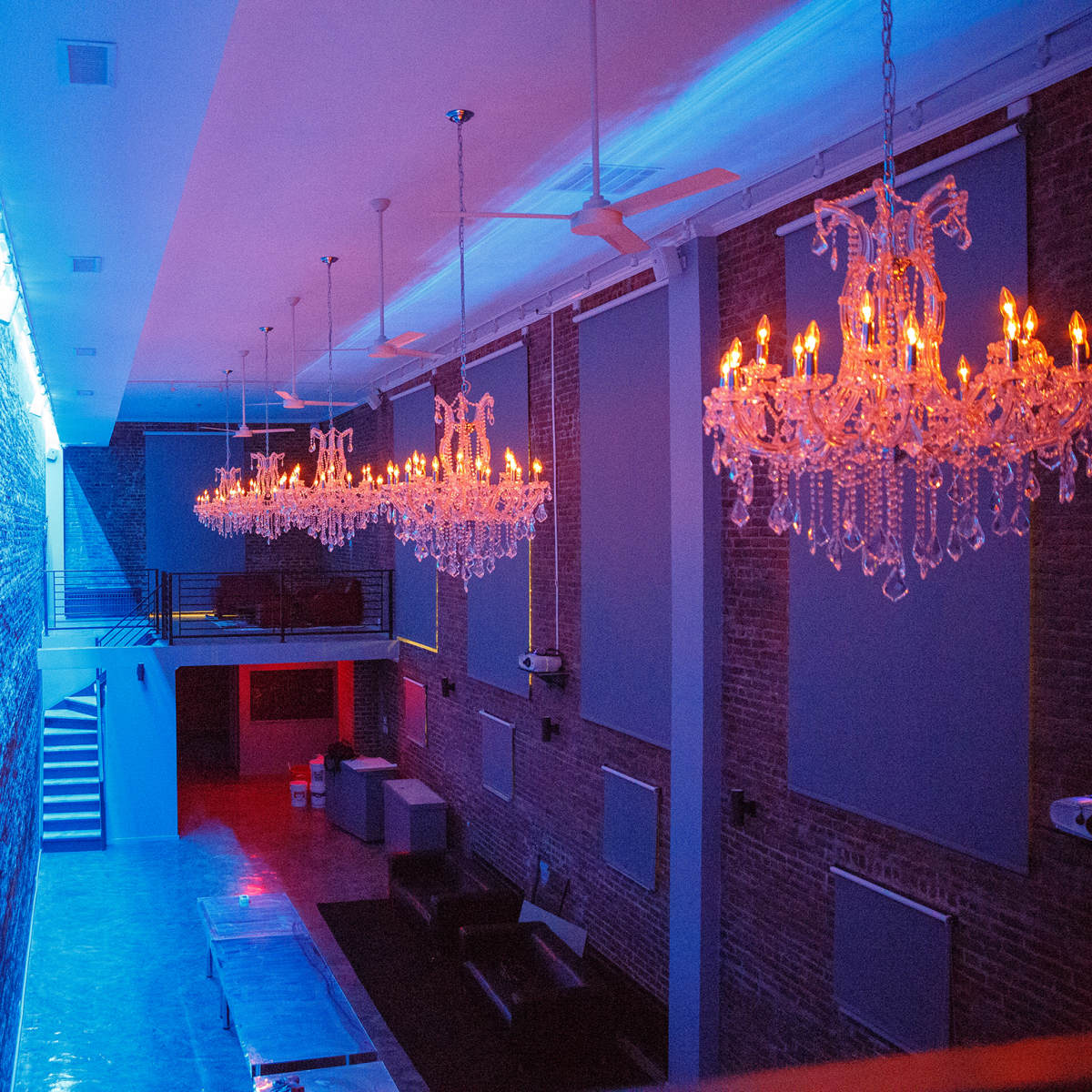 The scene shows a modern interior space with exposed brick walls, colorful lighting, and elegant chandeliers hanging from the ceiling.