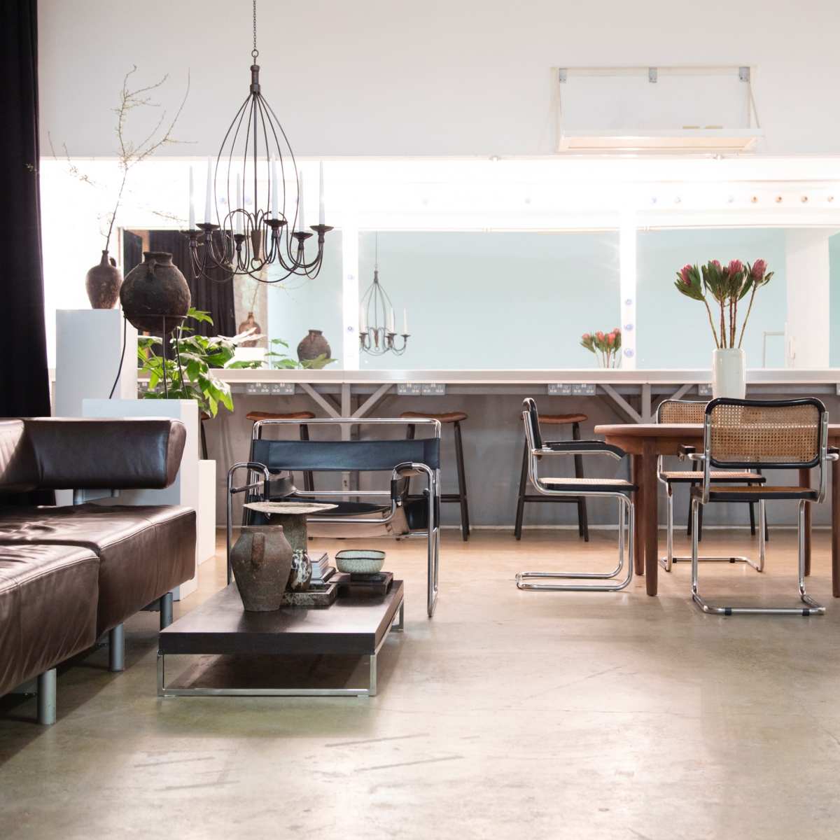A spacious interior features a dark leather sofa, a wooden dining table surrounded by modern chairs, and a bright countertop with decorative plants and tableware.
