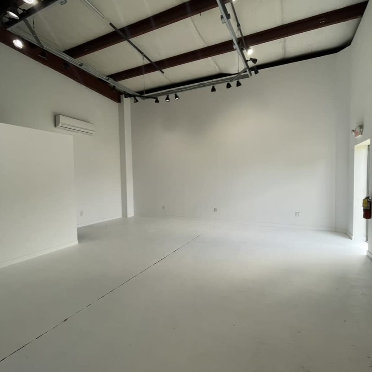 A spacious, empty room with white walls and a concrete floor, featuring a doorway on one side.