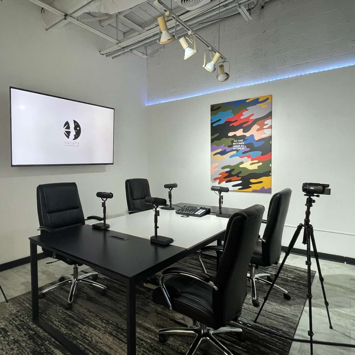 A modern conference room features a large display screen, a central table with chairs, and several cameras positioned on tripods.