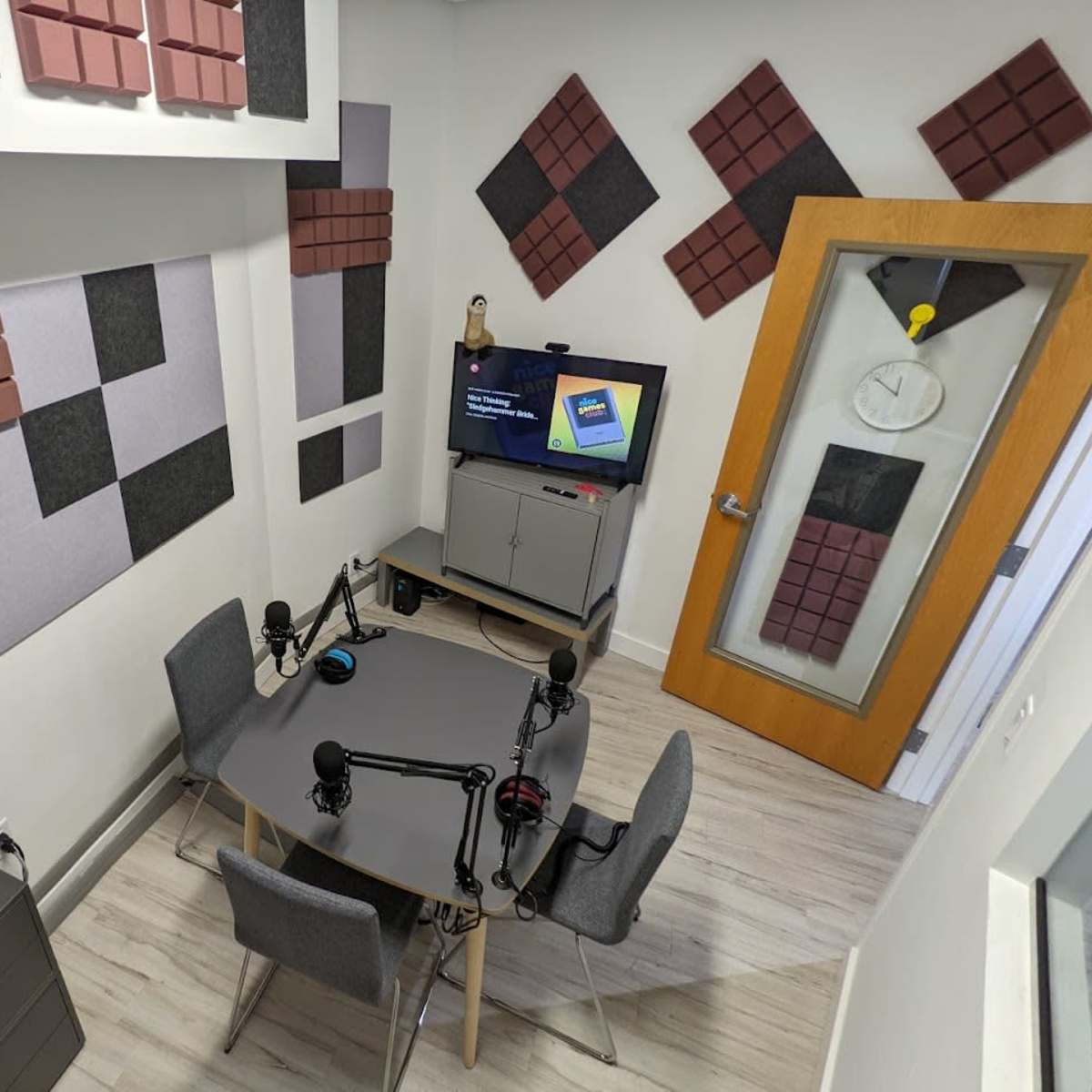 A soundproof recording studio with a table, four microphones, and a television displaying content on a wall with acoustic panels.
