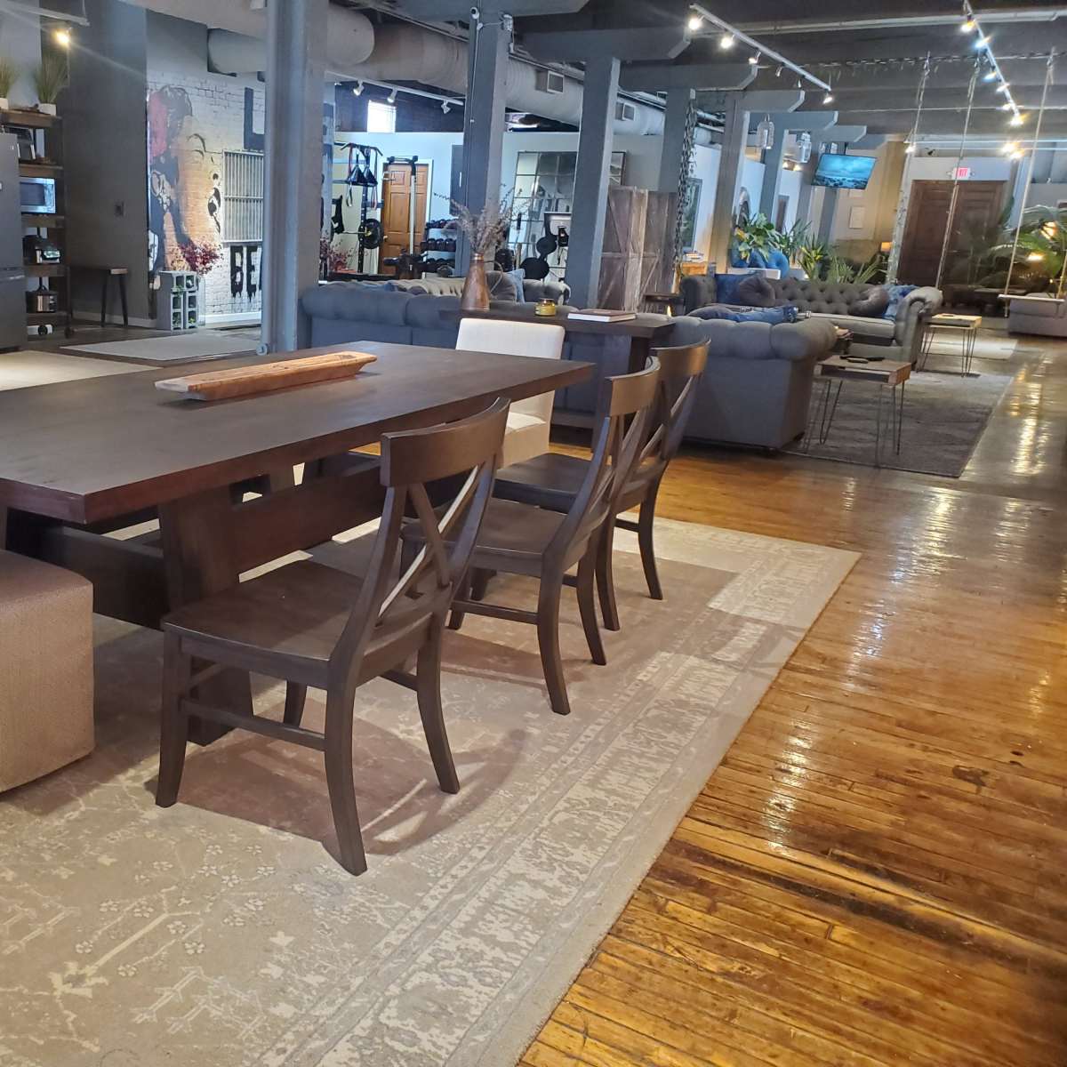 A large wooden dining table with six chairs is set on a patterned rug in a spacious room filled with modern furniture and decor.