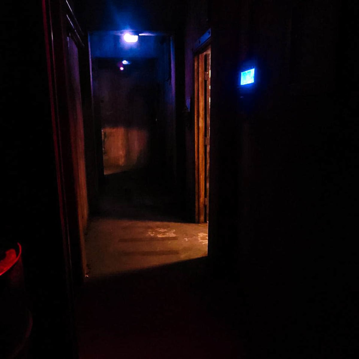 A dimly lit hallway with faint blue and red lights at either end, leading to closed doors on each side.