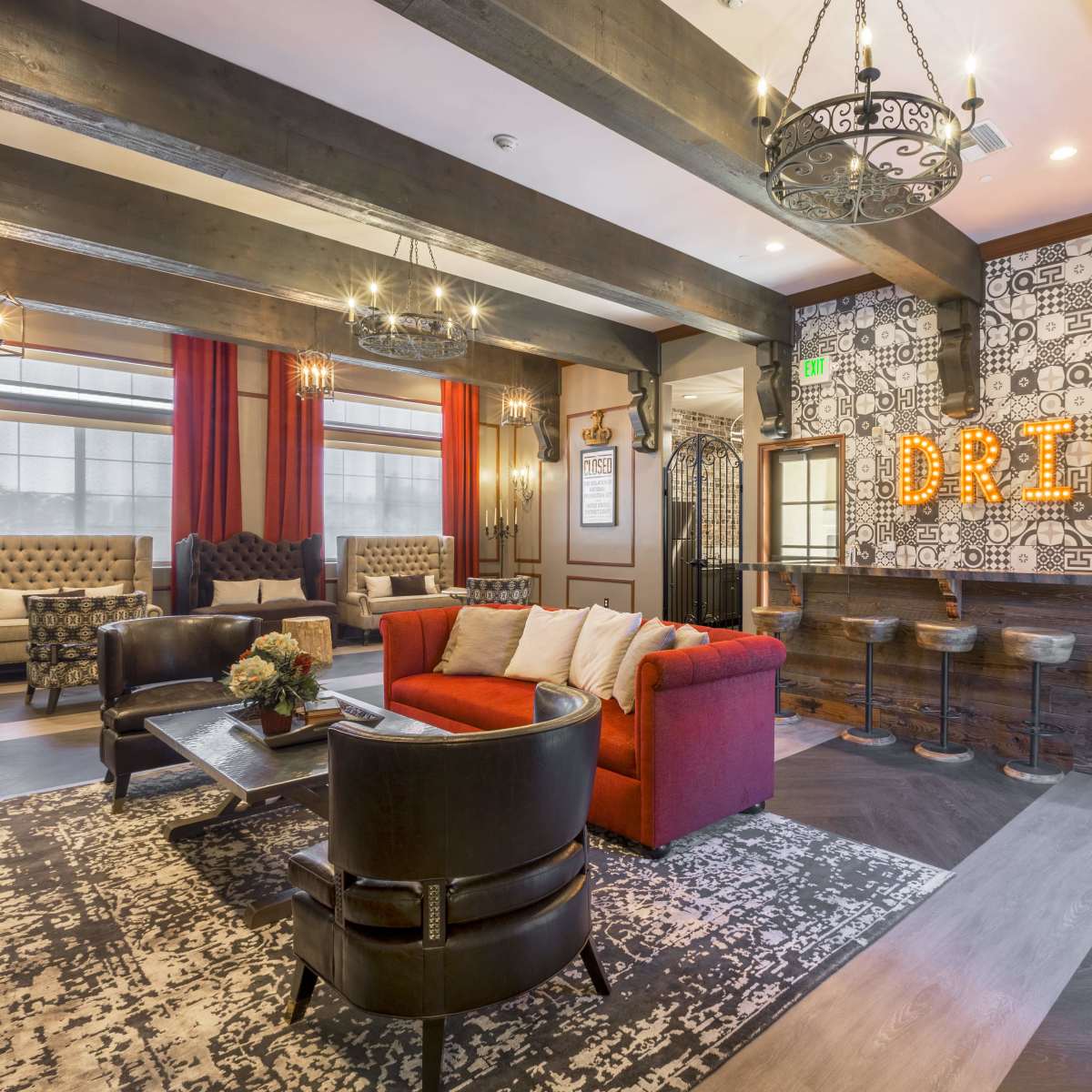 A lounge area with red chairs, a dark wood bar, and bold "DRINK" signage on a patterned wall.