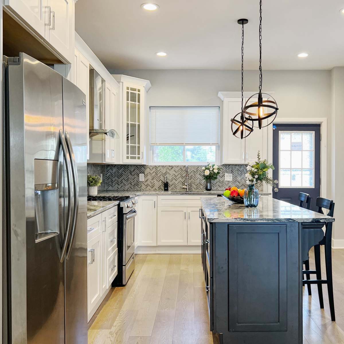 A modern kitchen with white cabinets, a dark island, and stainless steel appliances.