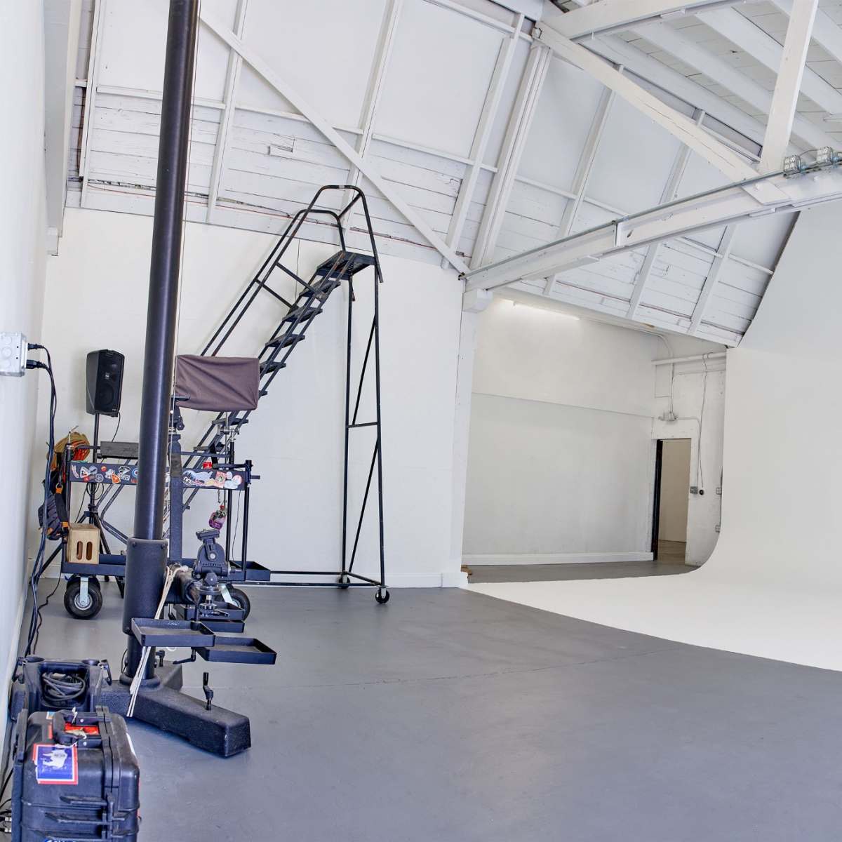 A spacious photography studio with a seamless white backdrop, gray flooring, and an open door allowing natural light to enter.