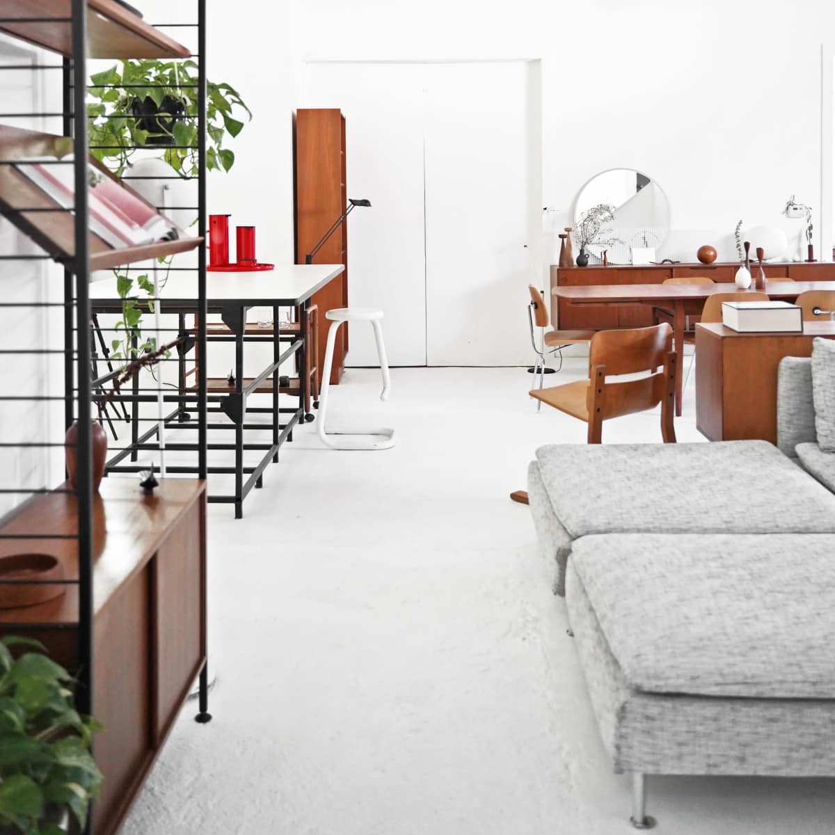 A modern, open-concept interior featuring a mix of wooden furniture, a minimalist shelving unit, and greenery.