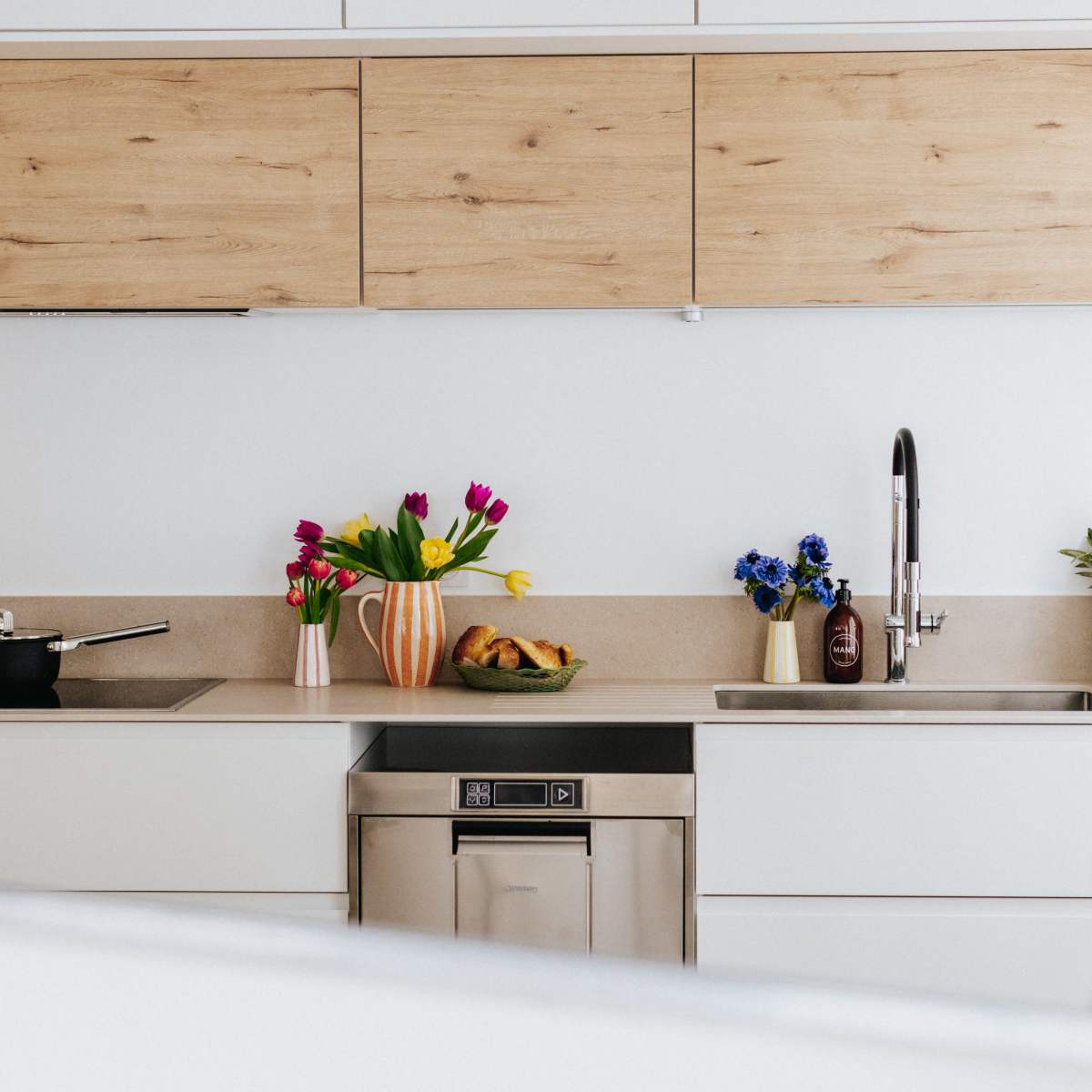 A modern kitchen features wooden cabinets, stainless steel appliances, and a variety of colorful flowers in vases on the countertop.