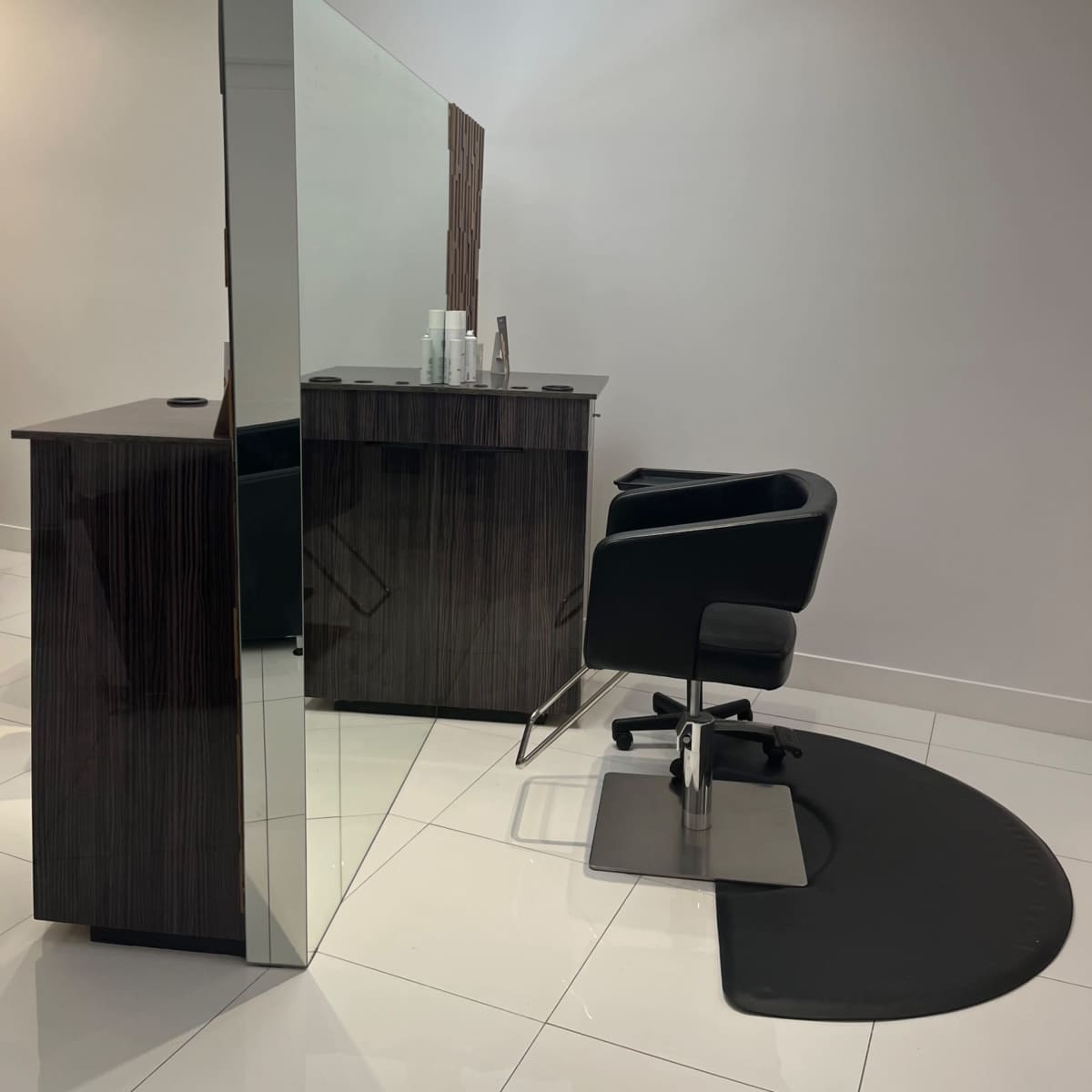 A modern hair salon with a black styling chair and a mirrored partition separating the styling area from the rest of the space.