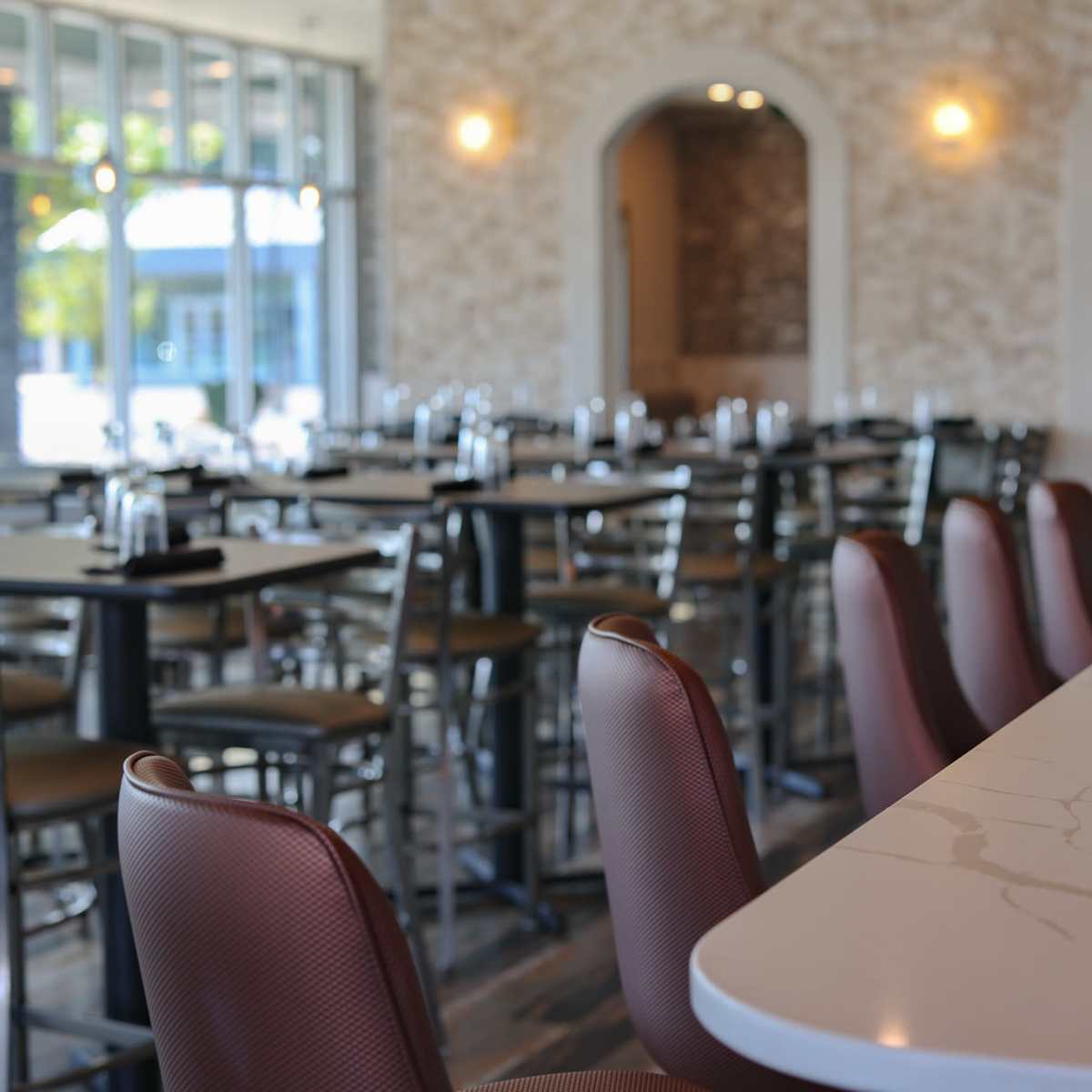 An empty dining area of a restaurant with rows of tables and chairs, and a long marble countertop in the foreground.