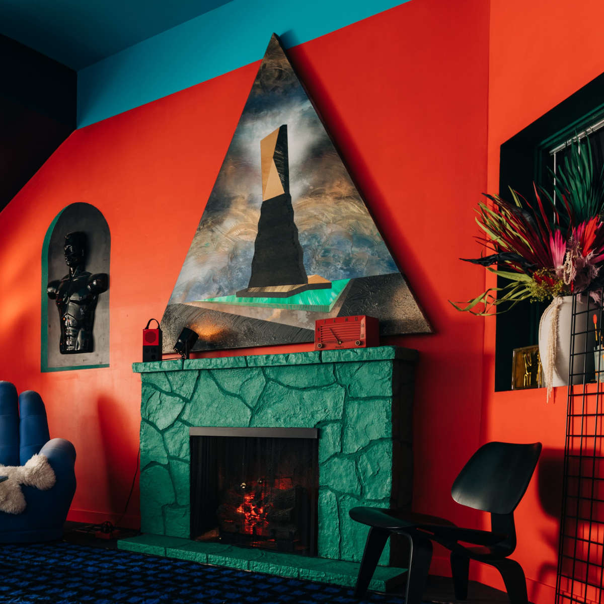 A vibrant interior featuring an orange wall, a teal ceiling, a green stone fireplace, and a large triangular painting above it.