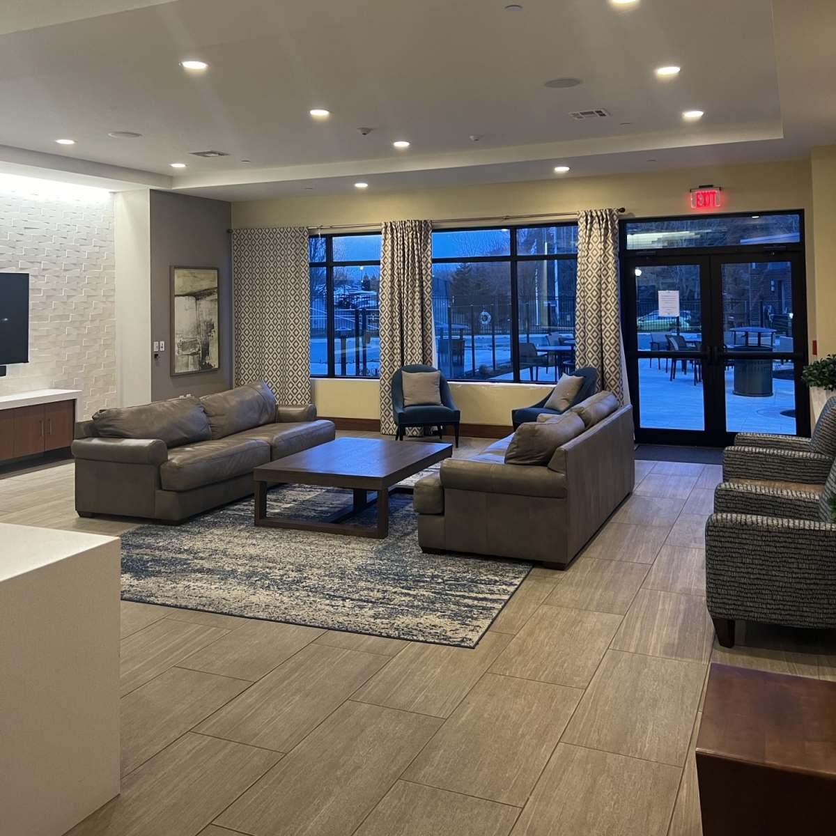 A modern lobby area featuring two sofas, a coffee table, and large windows with curtains, illuminating the space with natural light.