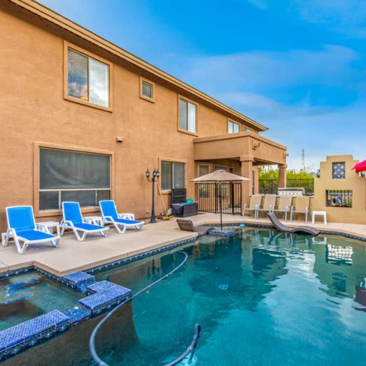 A backyard with a swimming pool surrounded by lounge chairs and a house with multiple windows.
