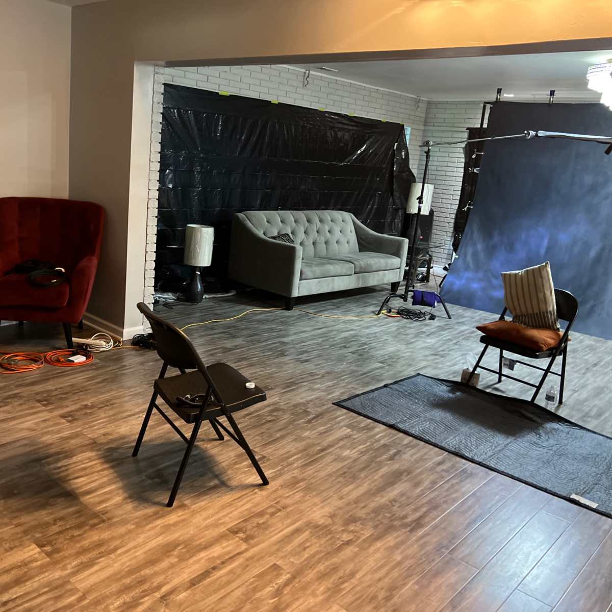 A professional studio space with a red velvet armchair, a gray couch, and various equipment set up for a photoshoot.