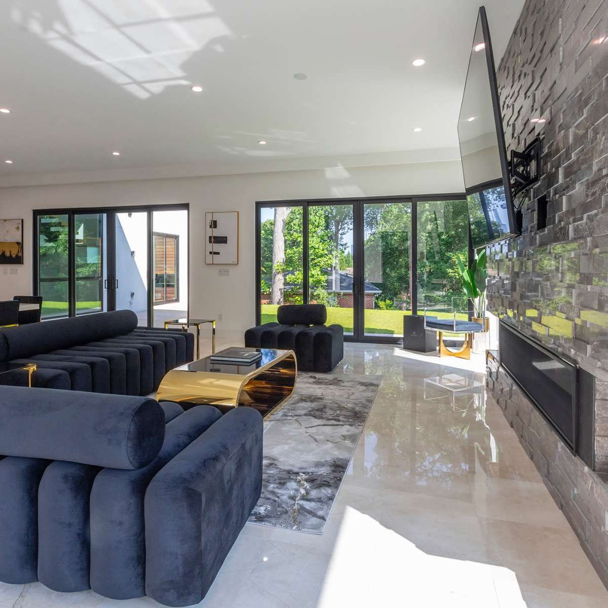 A modern living room featuring a black sectional sofa, a marble coffee table, and large glass doors leading to a garden outside.