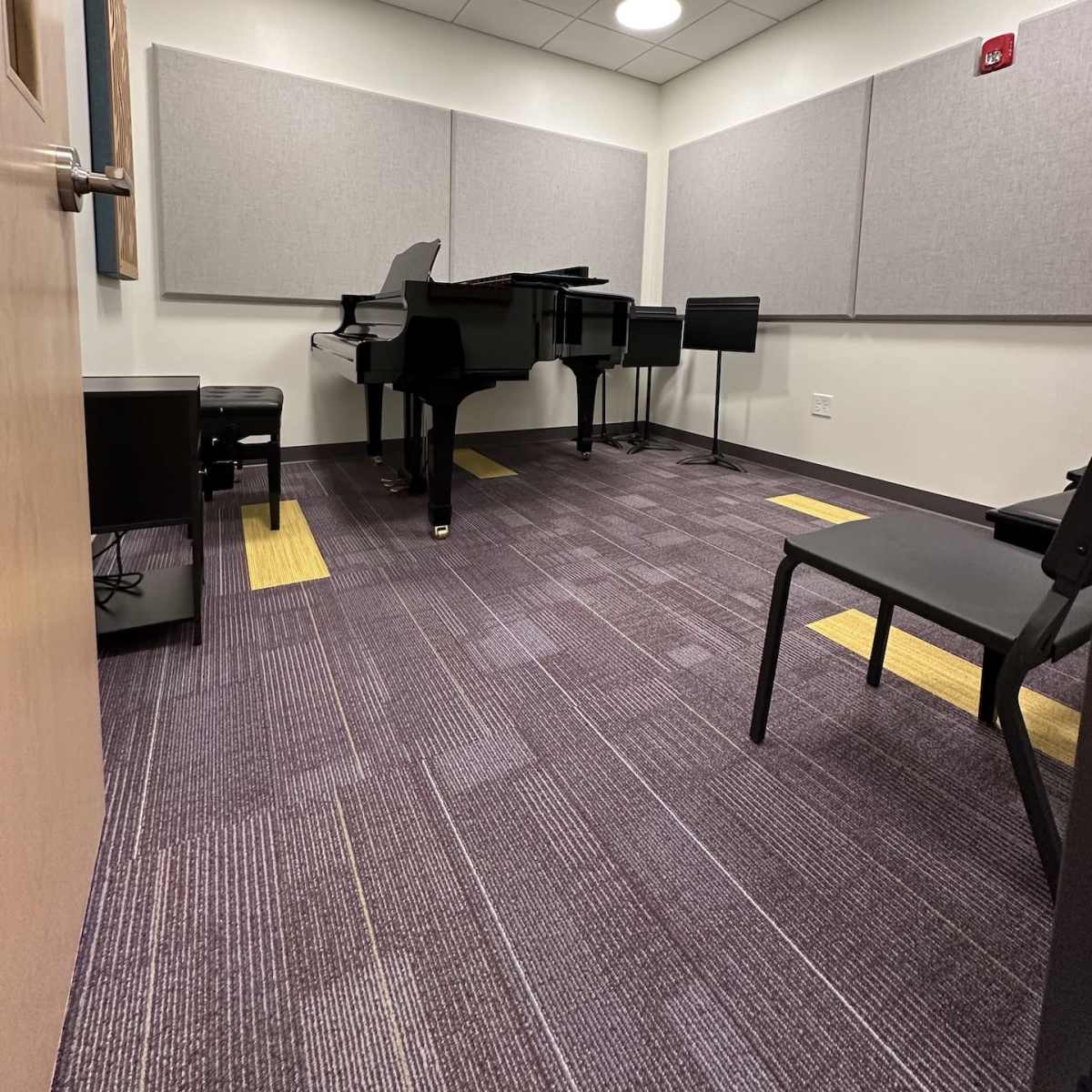 A soundproof room with a black grand piano, two chairs, and acoustic panels on the walls.