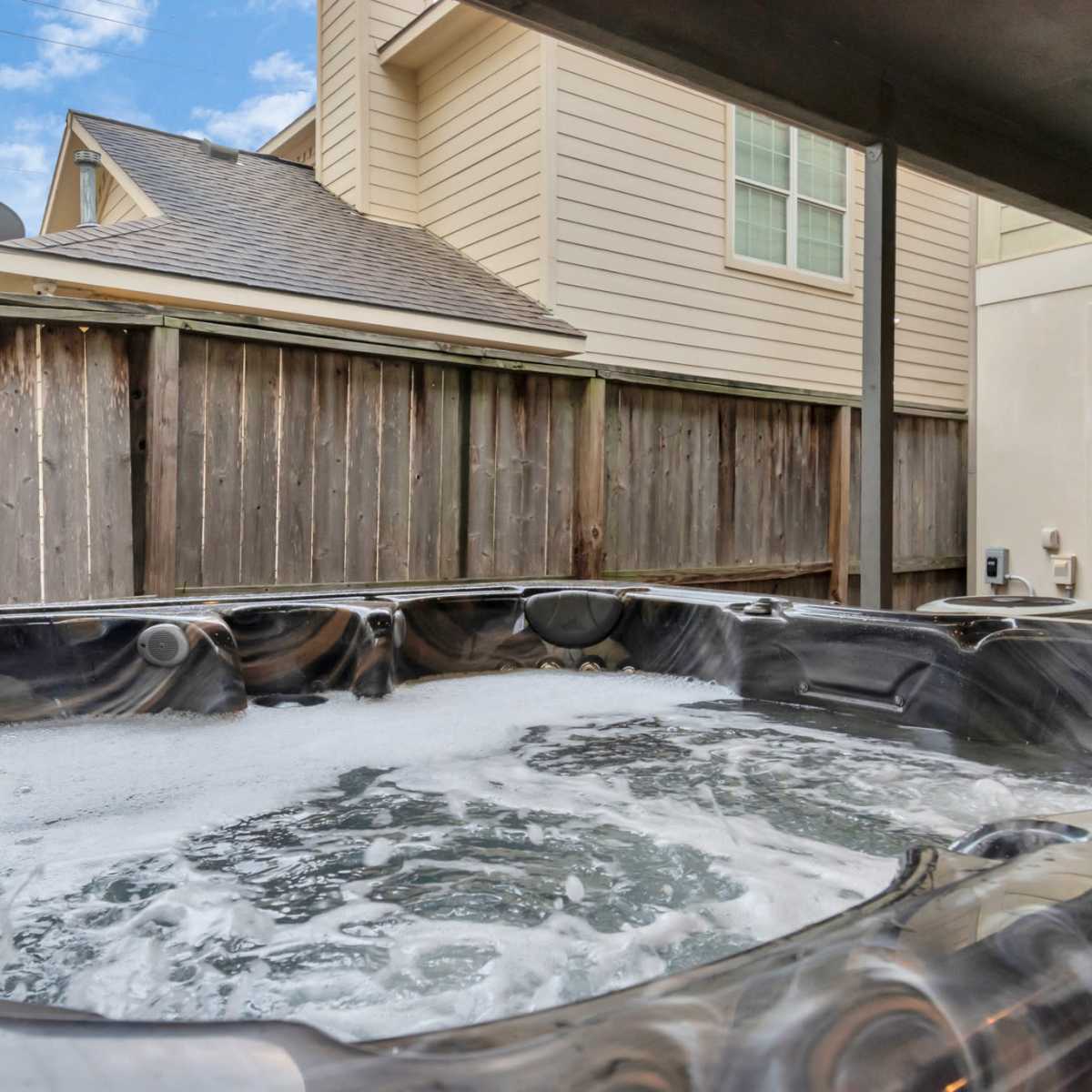 A hot tub filled with bubbling water, situated under a covered area near a wooden fence.