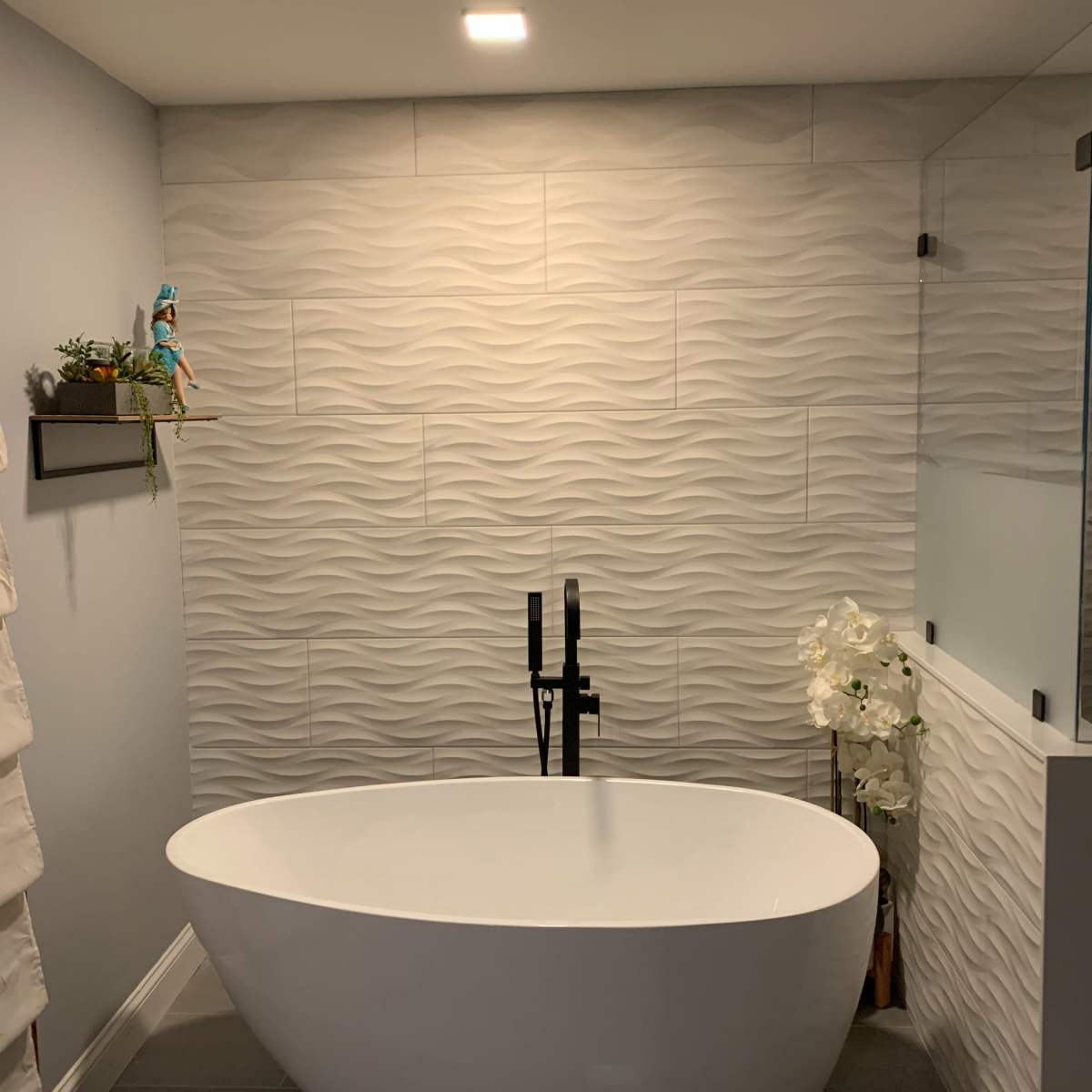A modern bathroom featuring a freestanding white bathtub, a textured wave-patterned wall, and a glass shower enclosure.