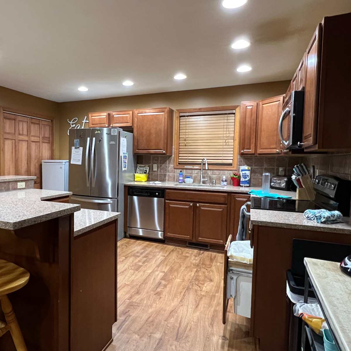 A kitchen with wooden cabinets, a stainless steel refrigerator, and a countertop with bar seating.