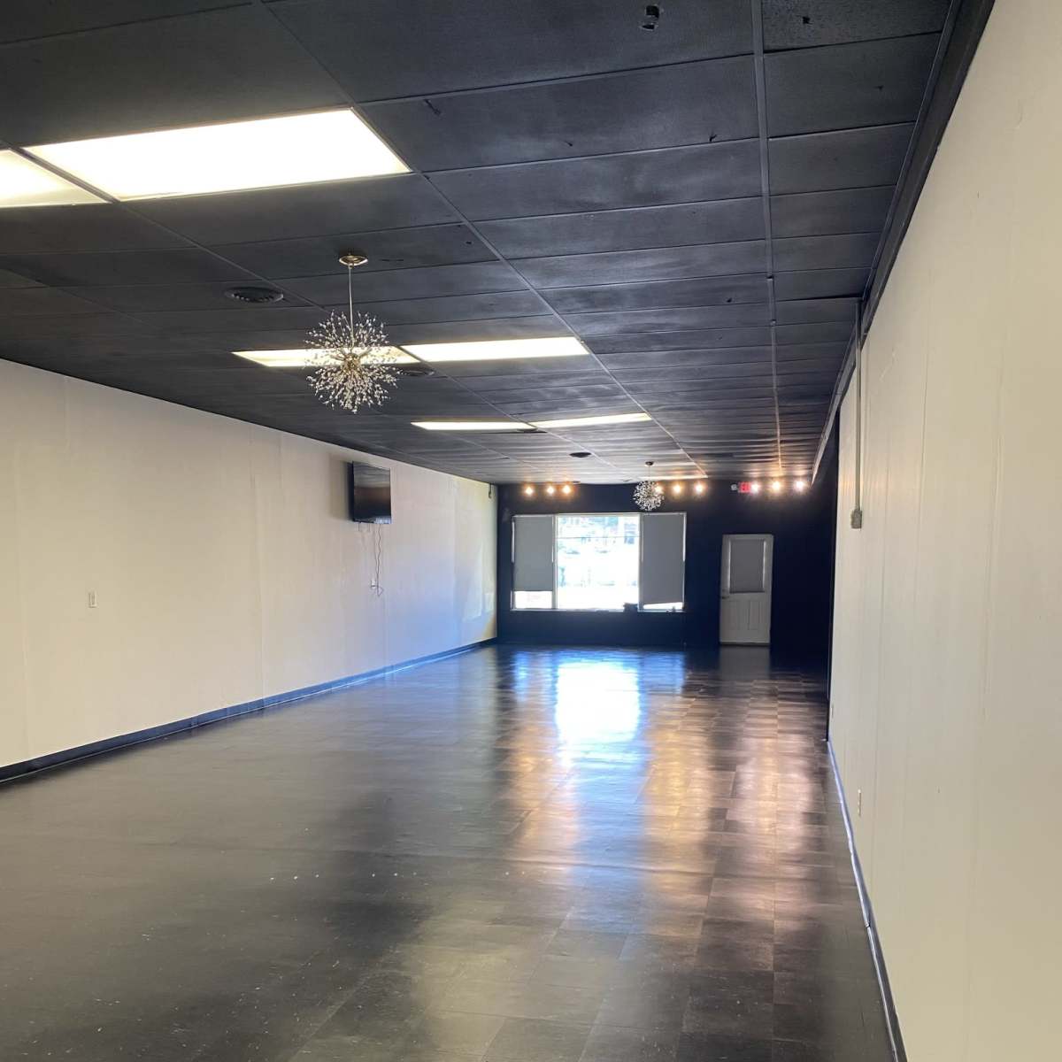 A spacious, empty room with black tile flooring, white walls, and an illuminated window at the far end.