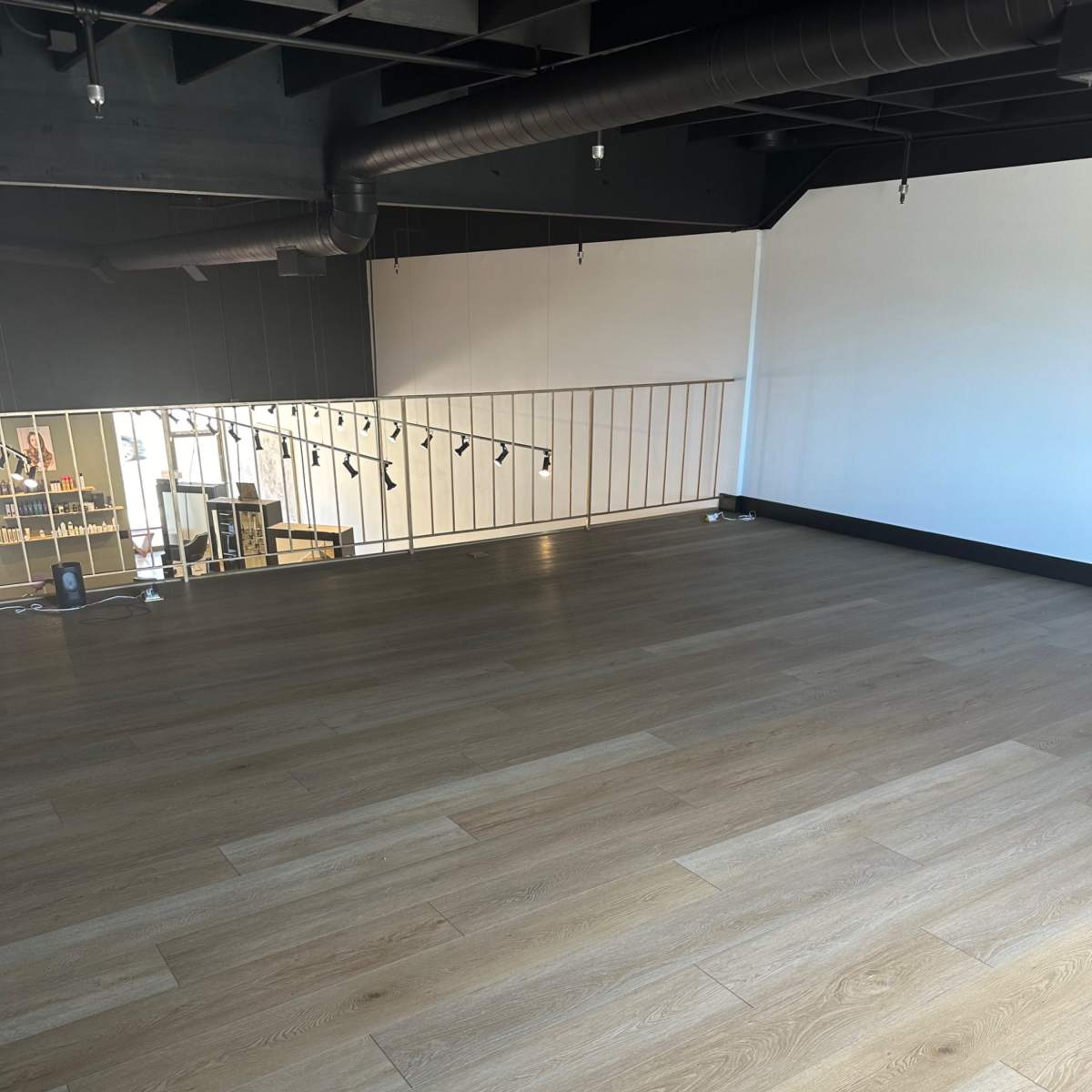 An empty room with wooden flooring and a railing along one side of the space.
