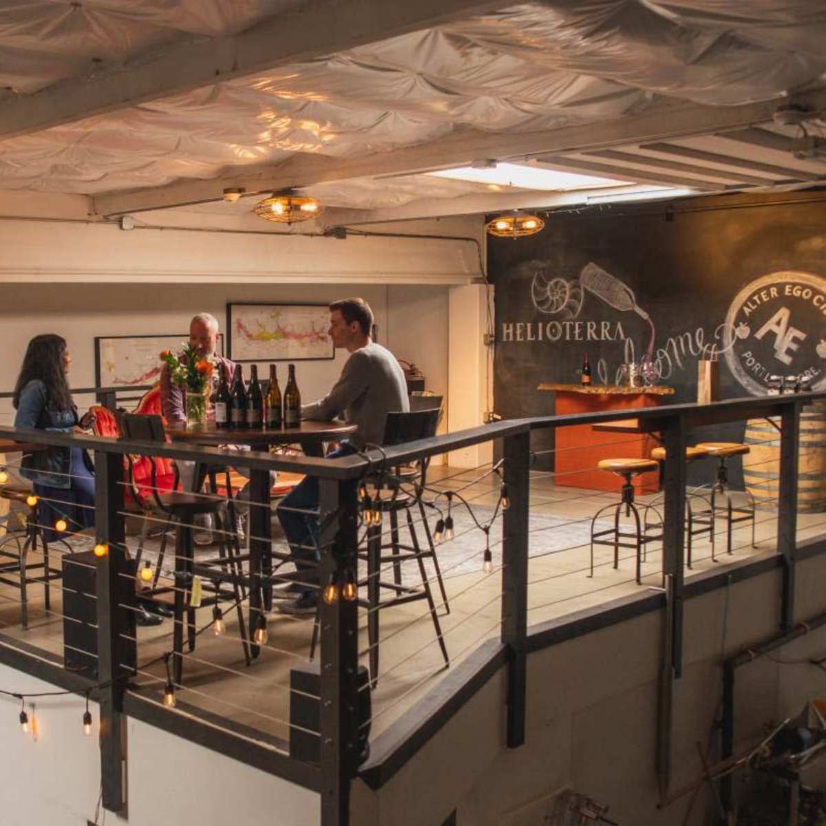 A group of three people sits around a table on an upper level of a spacious tasting room with bottles and wine-related decor.
