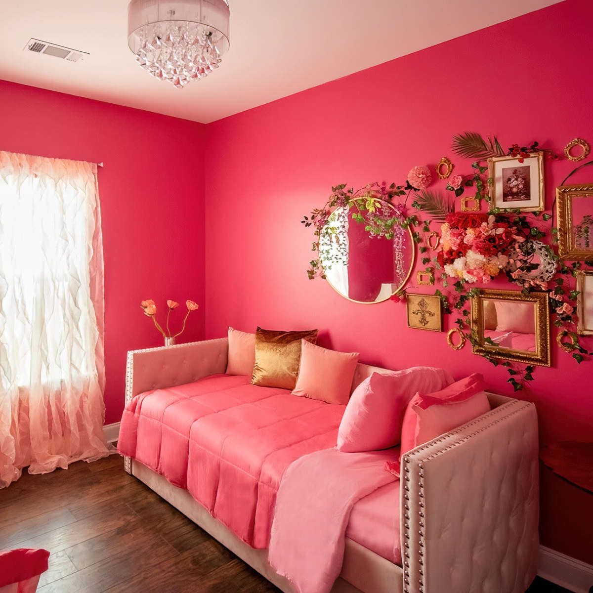 A pink-themed bedroom featuring two daybeds, a decorative mirror, and floral wall art.