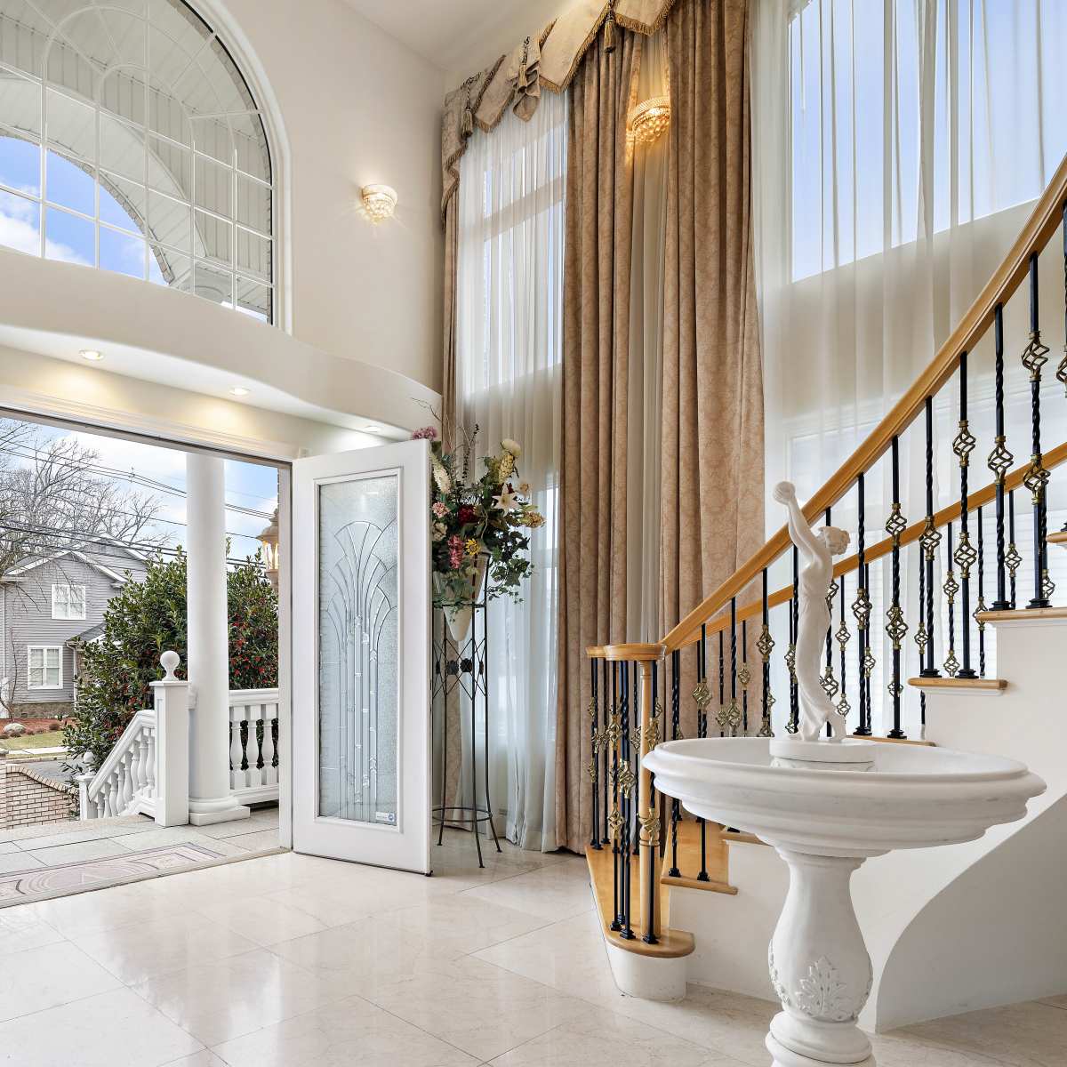 A spacious entryway features double glass doors opening to the outside, large windows allowing natural light, and a staircase leading to the upper floor.