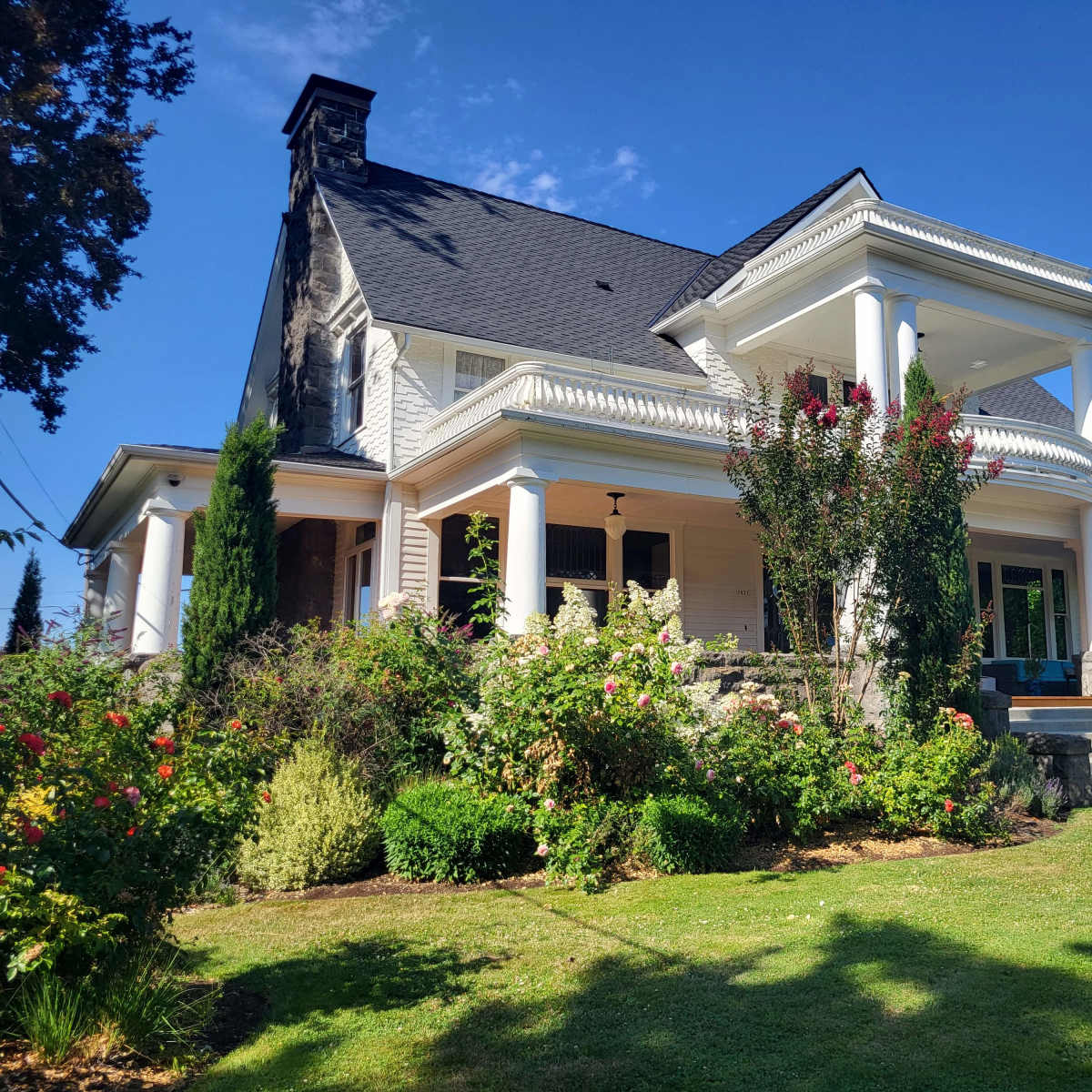 A large, two-story house with a porch, surrounded by well-maintained gardens and trees.