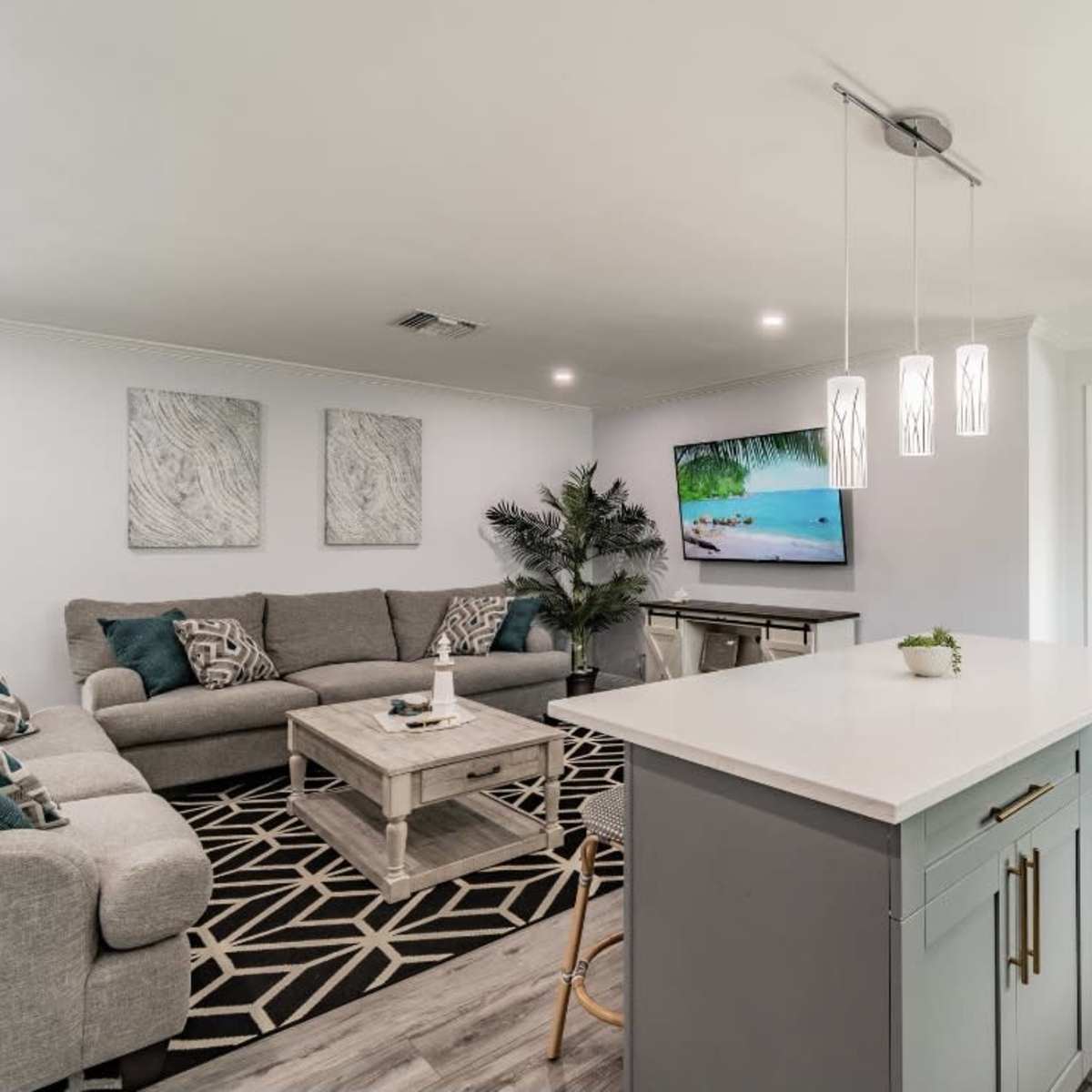 A modern living space featuring a gray sectional sofa, a coffee table, a wall-mounted TV, and a well-equipped kitchen island.
