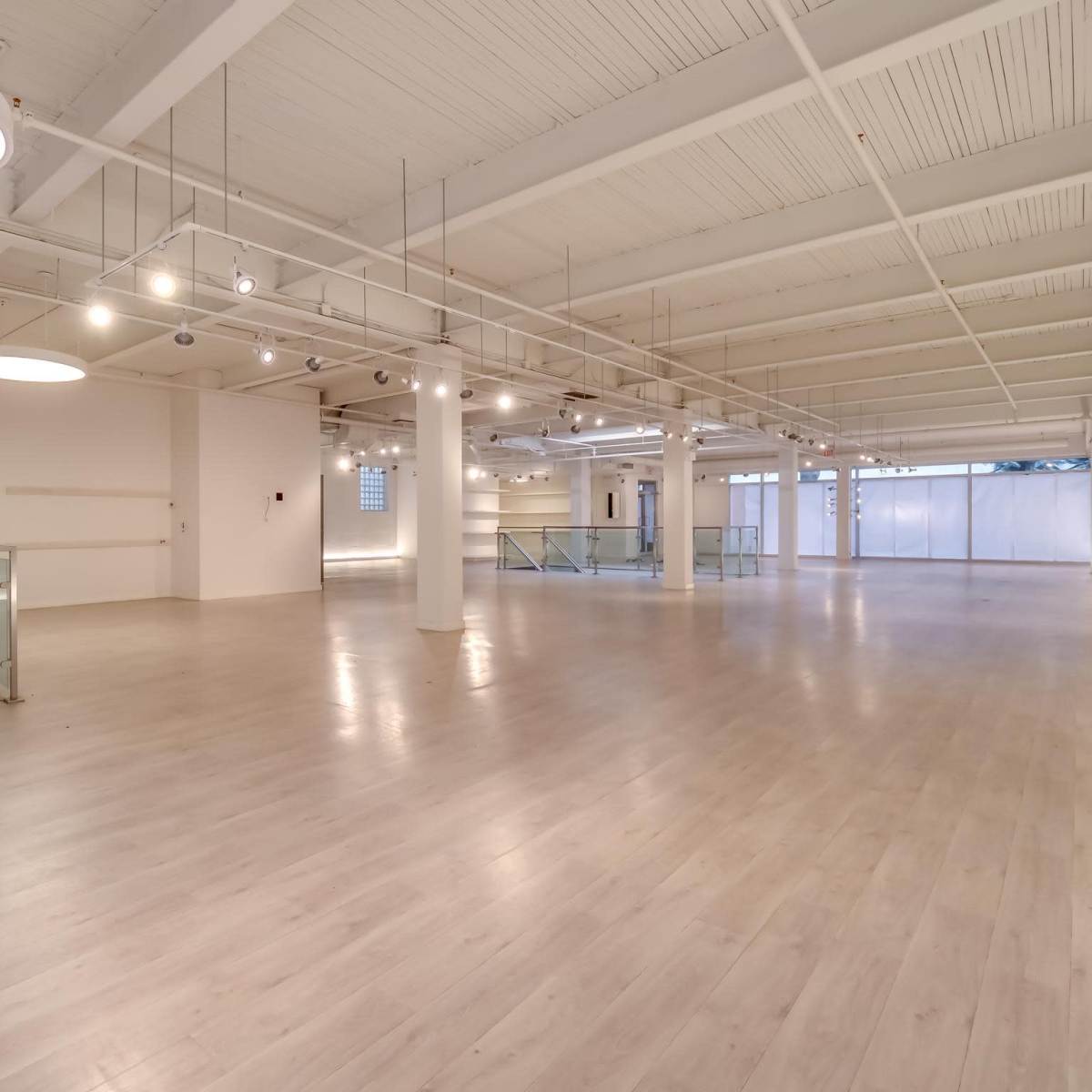 A spacious, empty interior with high ceilings, large windows, and polished wooden floors.