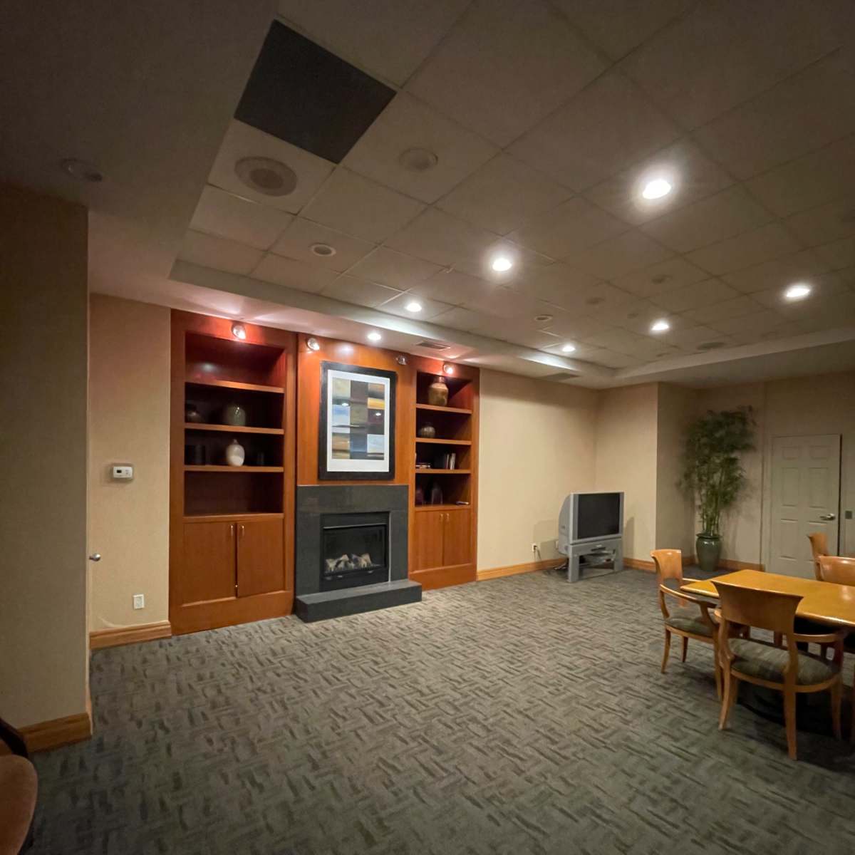 A well-lit room with a fireplace, built-in shelves, a television, and a dining table surrounded by chairs.