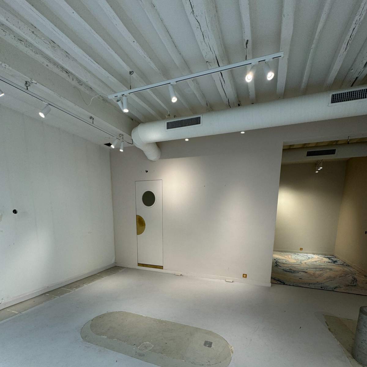A spacious, empty room with white walls, a circular door on the left, and a partially visible area in the back.