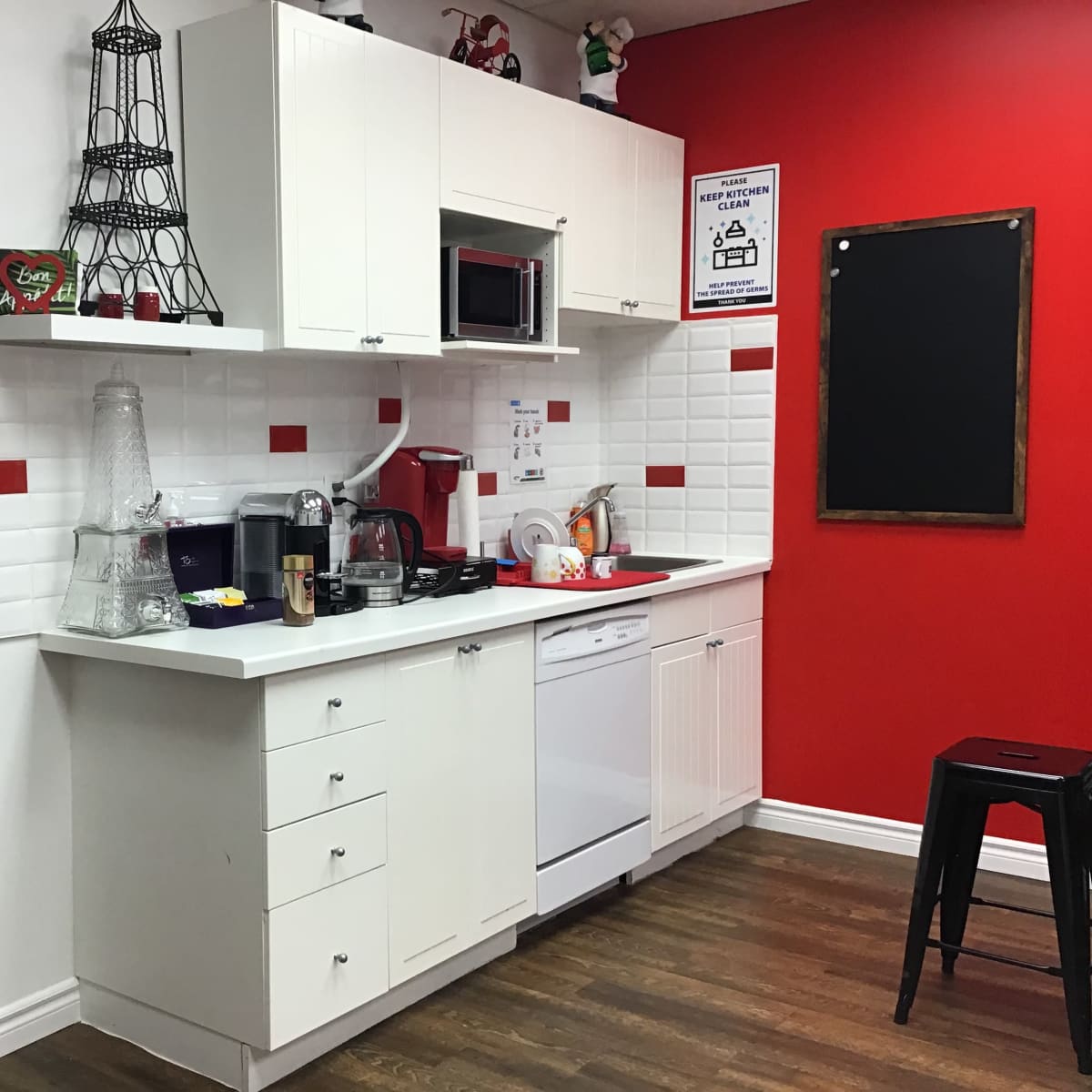 A compact kitchen with white cabinetry, a microwave, and various kitchen appliances against a red accent wall.