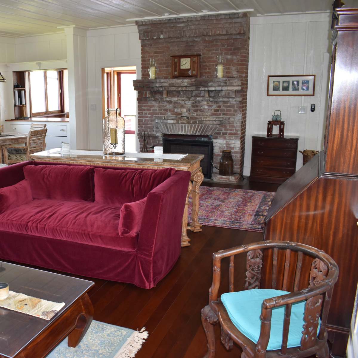 A cozy living room with a burgundy sofa, wooden furniture, a brick fireplace, and various decorative items arranged thoughtfully.