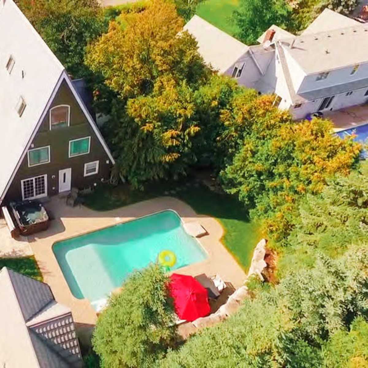 An aerial view of a property featuring a large A-frame house, a swimming pool, and surrounding greenery.