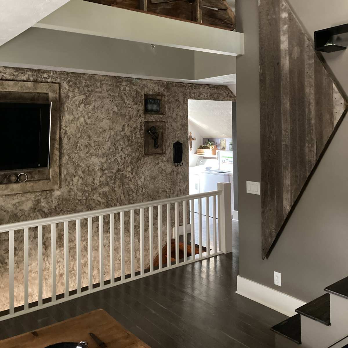 A modern interior space featuring a staircase, a textured wall with various decorations, and a glimpse of a kitchen in the background.