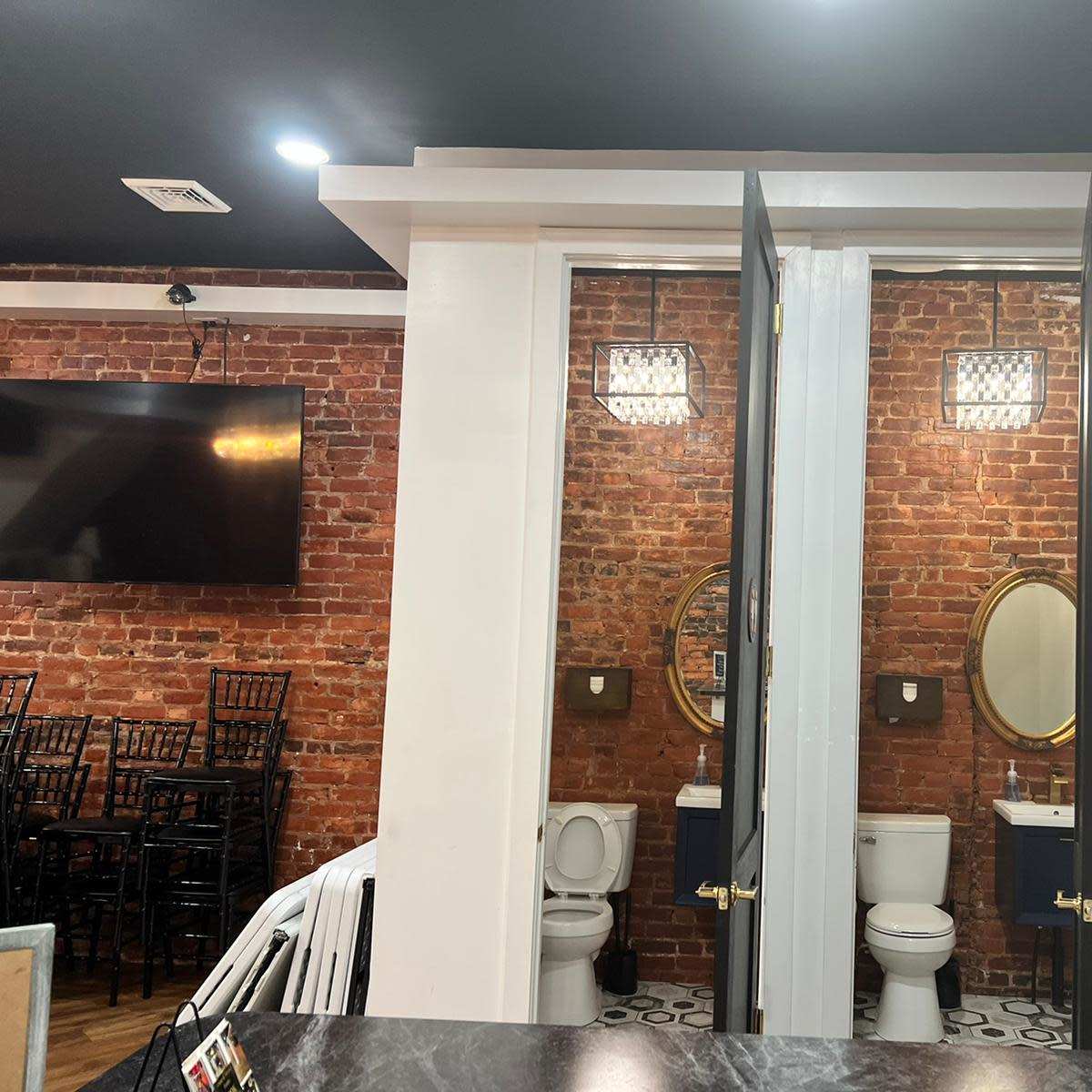 A modern restroom with two stalls, exposed brick walls, and decorative mirrors.