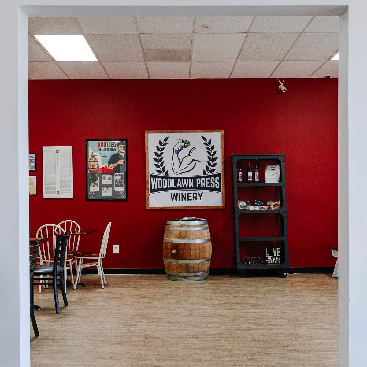 An interior view of a winery with red walls, a banner displaying "Woodlawn Press Winery," and wooden furniture.