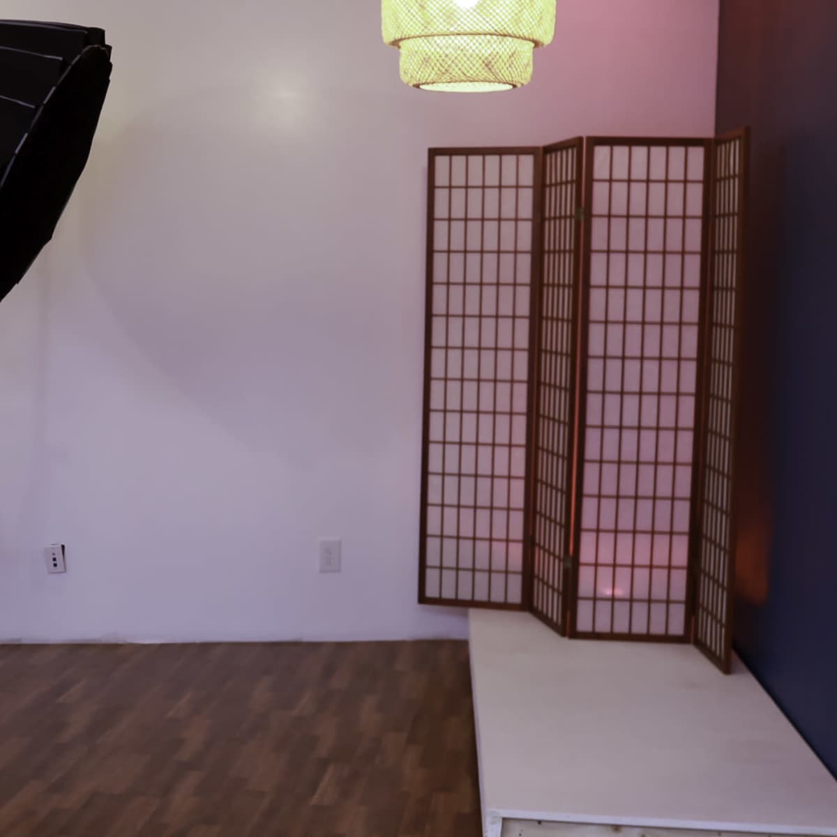 A photography studio with a large softbox light, a folding screen, and a wooden floor.