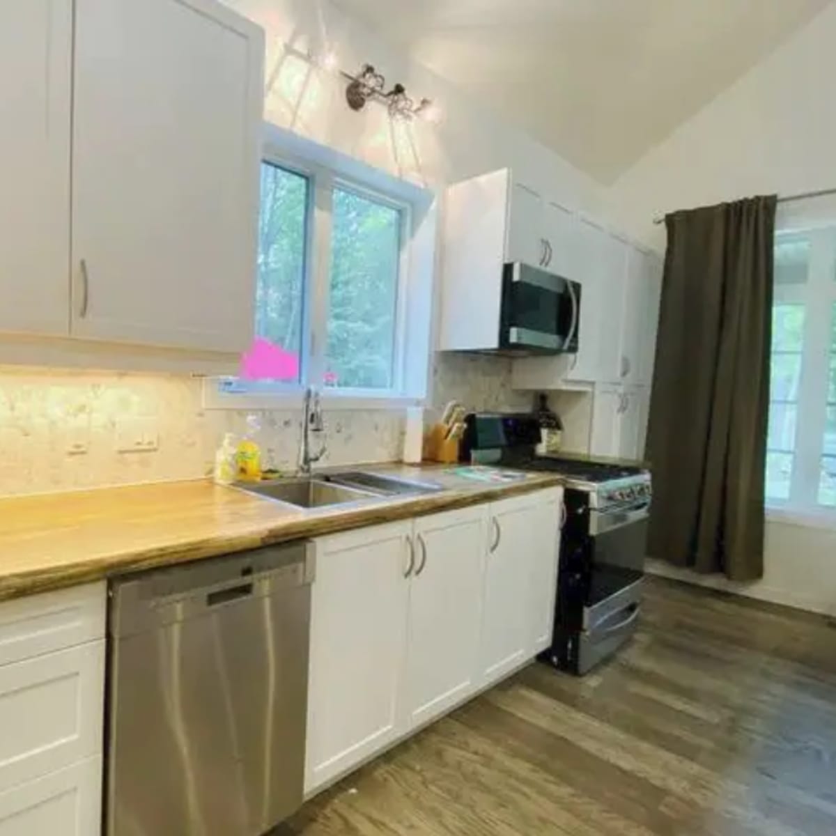 A modern kitchen featuring white cabinets, a wooden countertop, stainless steel appliances, and a window over the sink.