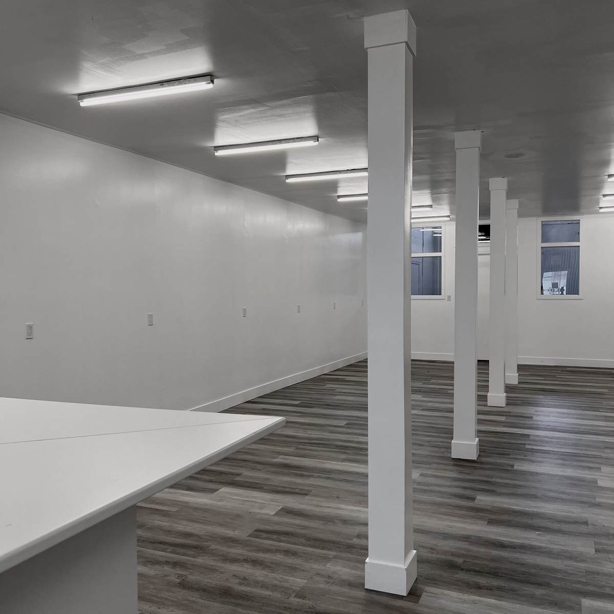 An empty room with white walls, a wooden floor, and several white columns supporting the ceiling.