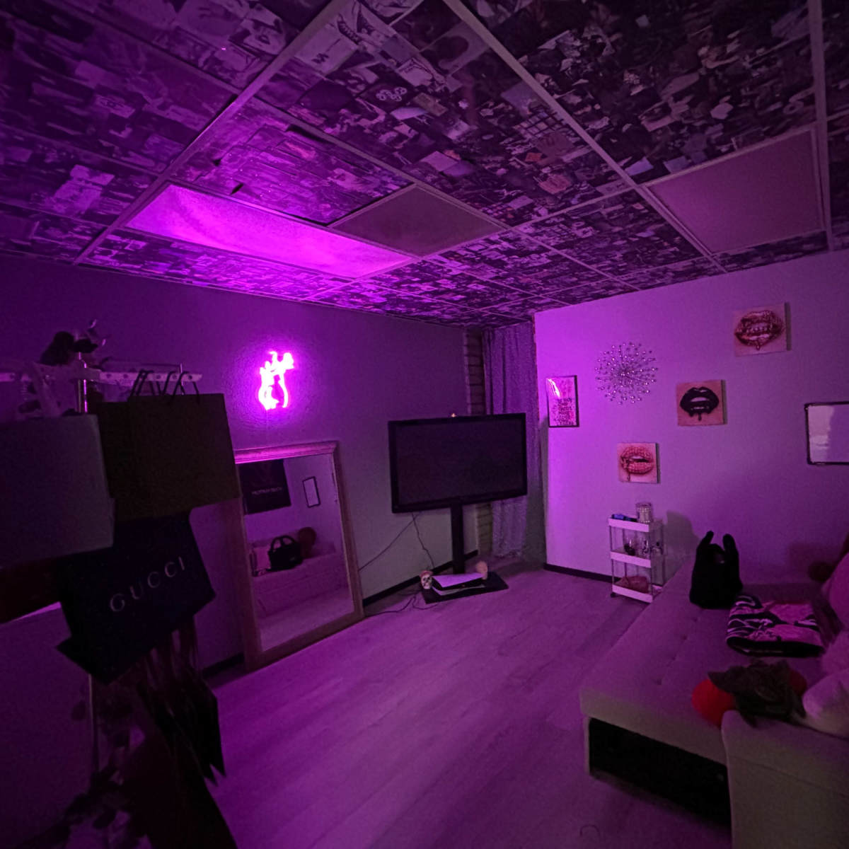 A dimly lit room features a couch, a television, and walls adorned with artwork, illuminated by a purple neon light.