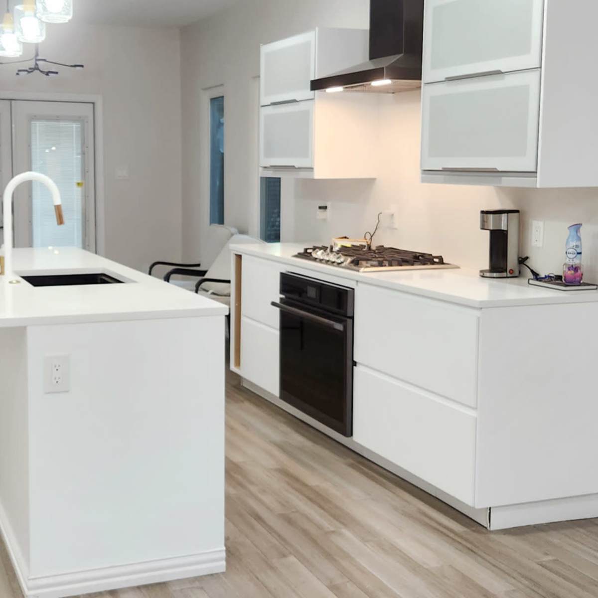A modern kitchen features a white island with a sink, a gas stove, and minimalistic cabinetry in a bright, open layout.