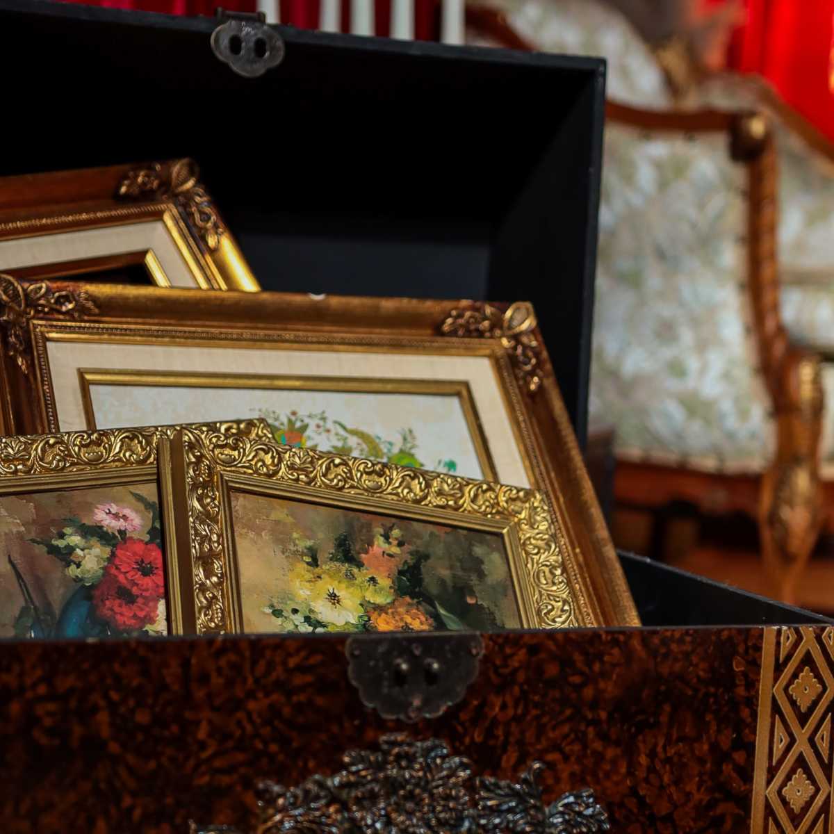 A decorative wooden box contains several framed paintings, while a couch and tall candles are visible in the background.