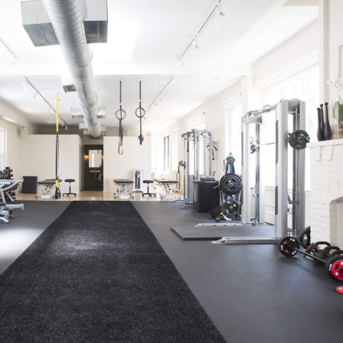 A spacious gym featuring various workout machines, cardio equipment, and free weights arranged along a central black carpeted pathway.