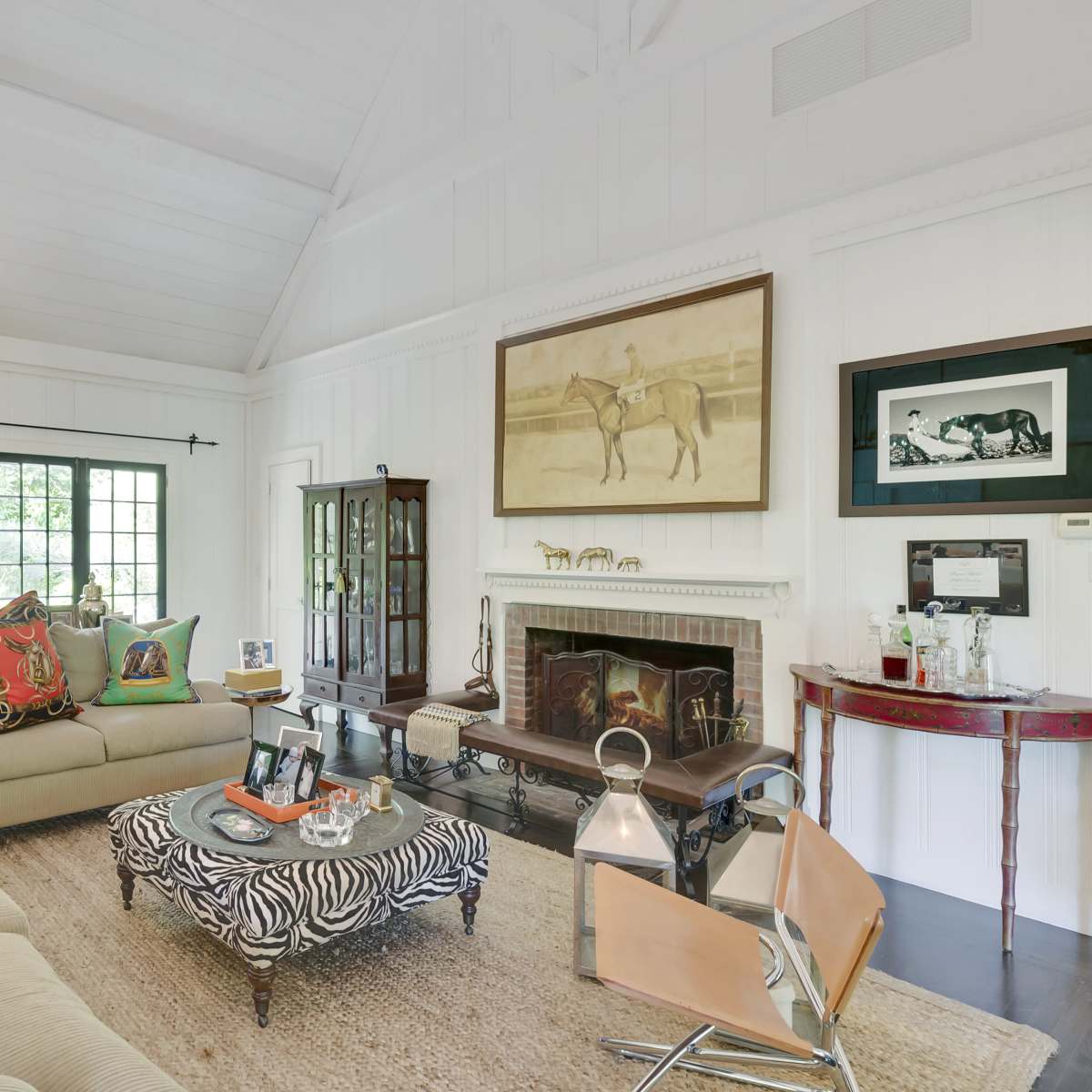 The living room features a large sectional sofa with colorful cushions, a zebra-patterned coffee table, and a fireplace surrounded by framed artworks.