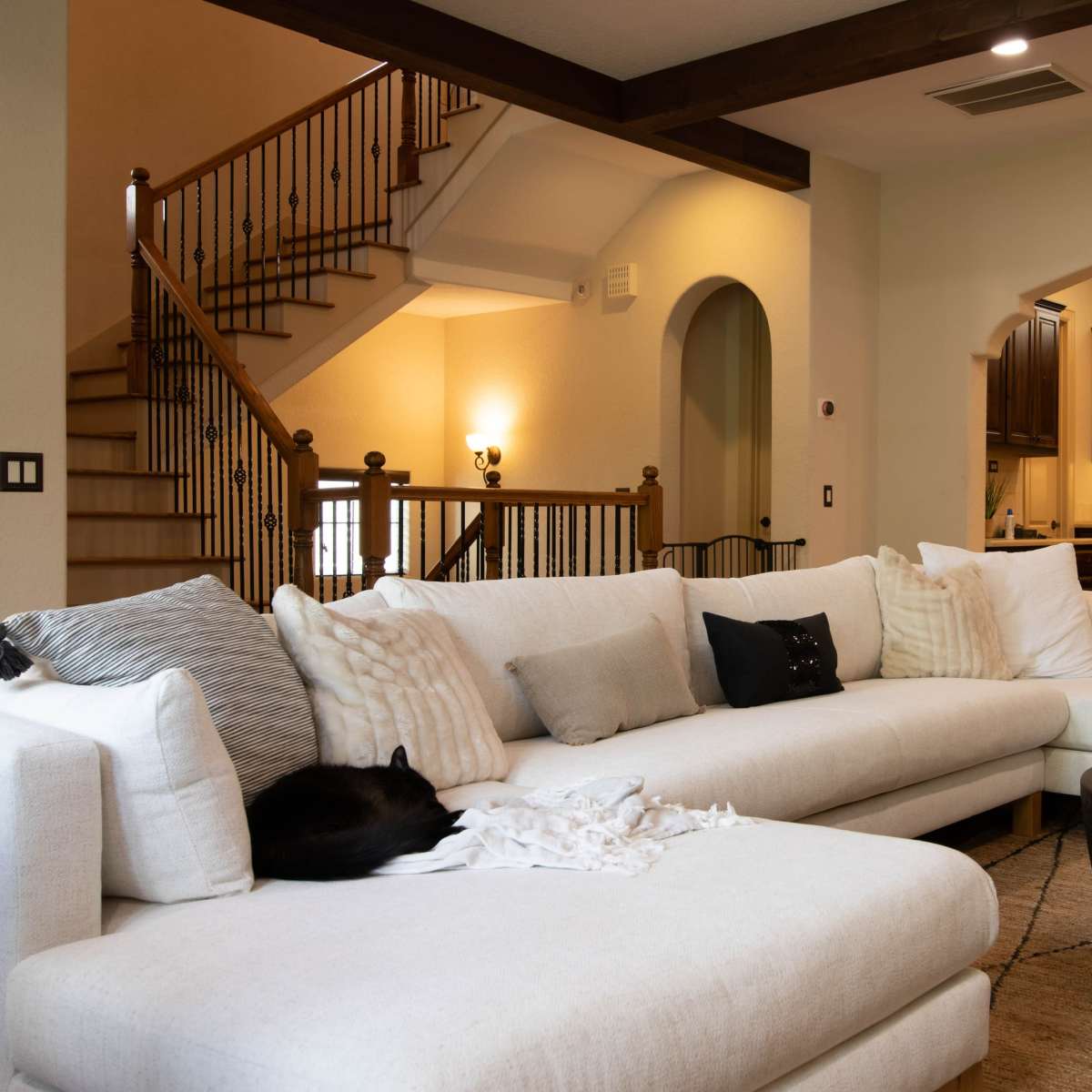 A modern living room features a large sectional couch, a round coffee table, and a view of a staircase leading to an upper level.