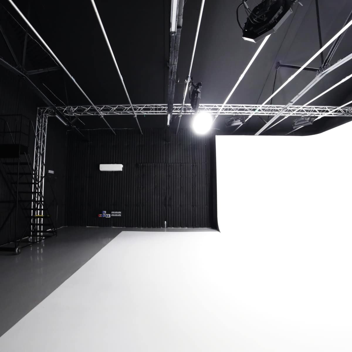 A minimalist studio space with a predominantly white backdrop, black walls, and a staircase in the corner.